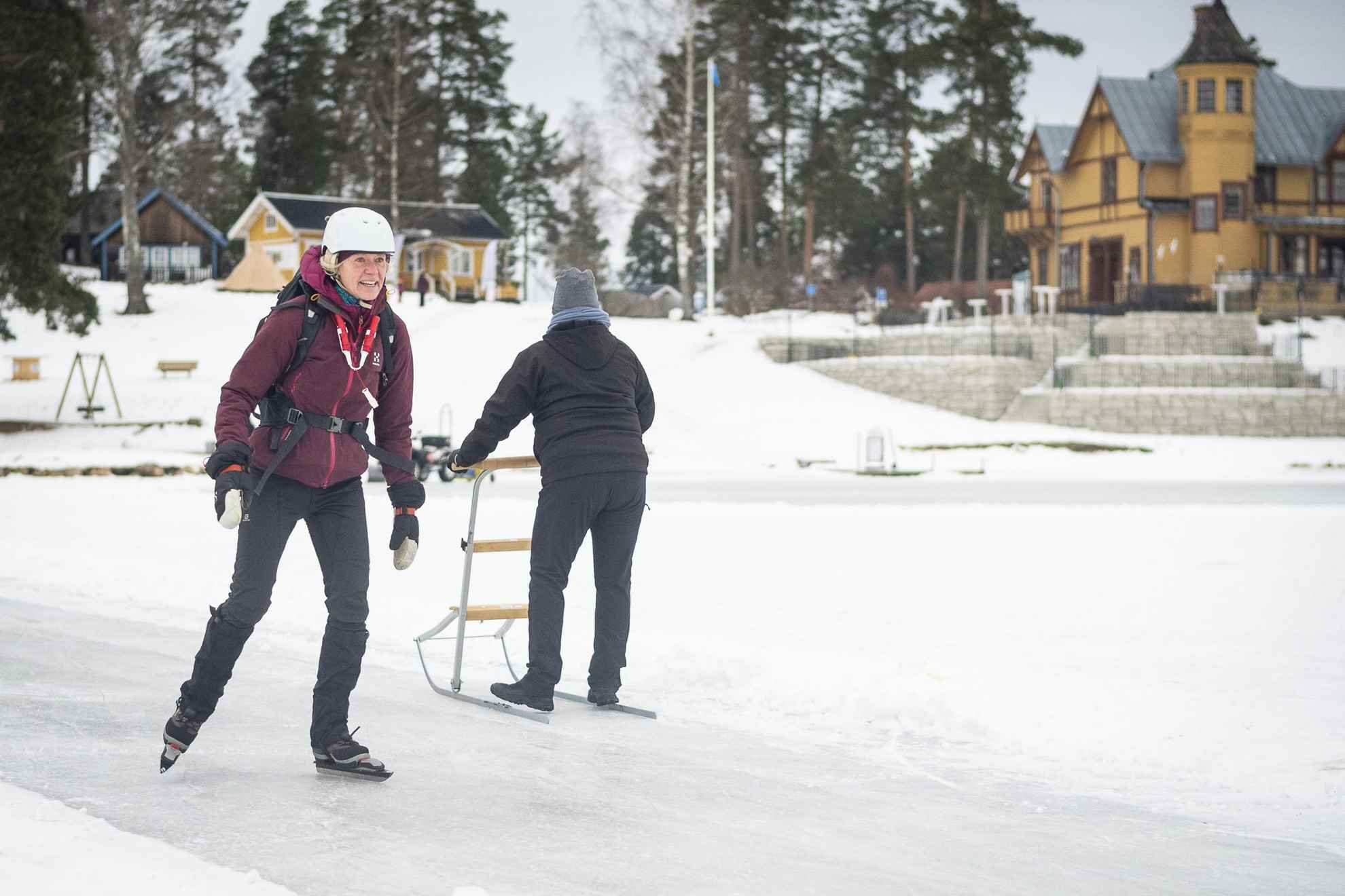 Une femme patine sur de longues distances tandis qu'une autre personne derrière elle fait du traîneau à neige sur la glace.