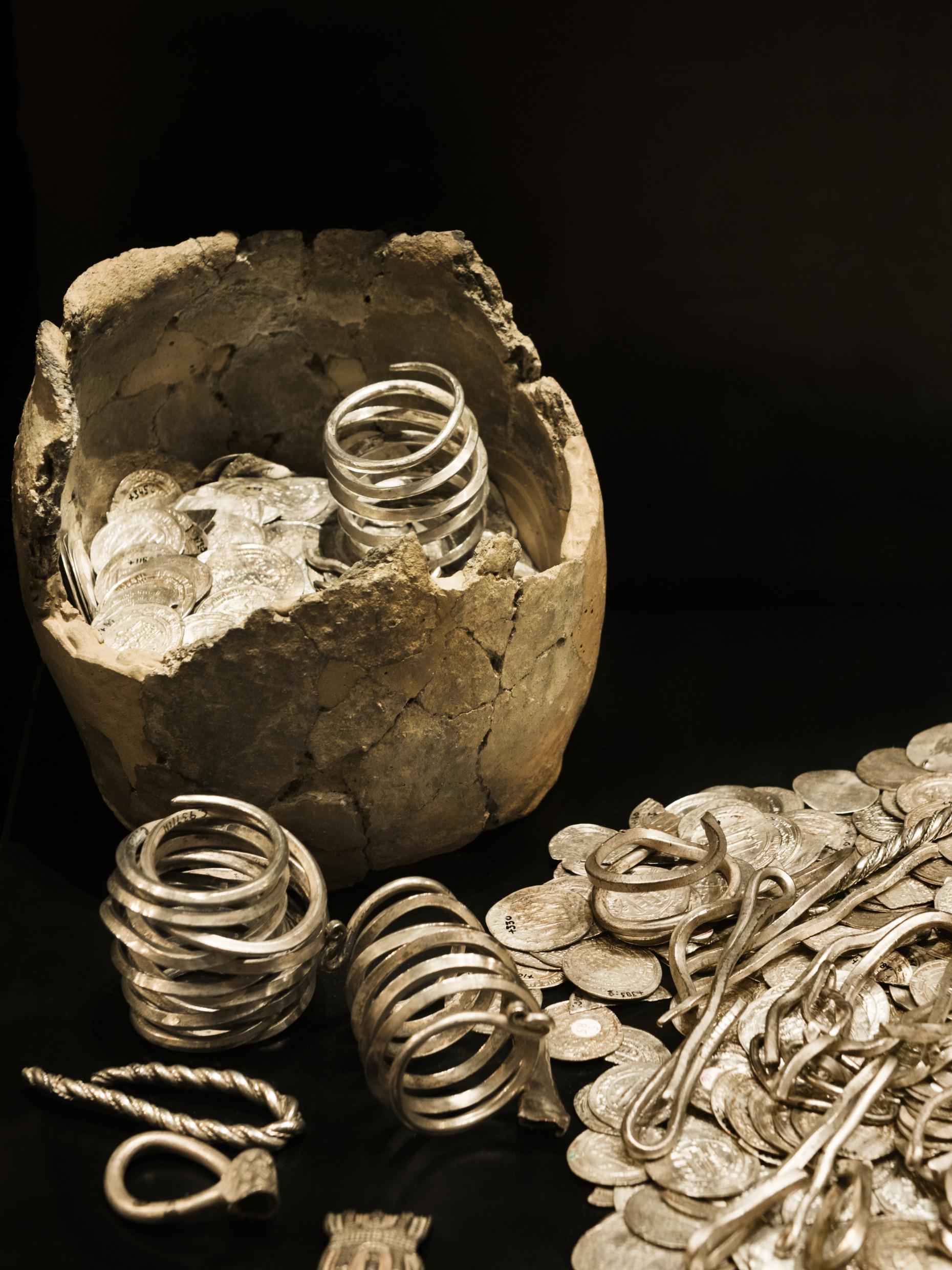 D'anciennes pièces en or et en argent et des bijoux sont posés sur une surface noire.