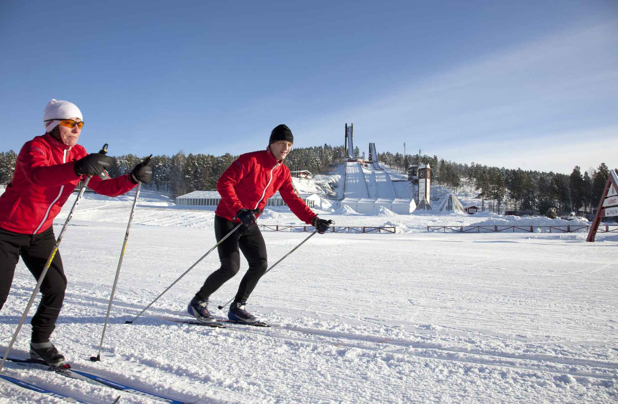 Deux personnes en veste rouge font du ski de fond sur des pistes préparées.