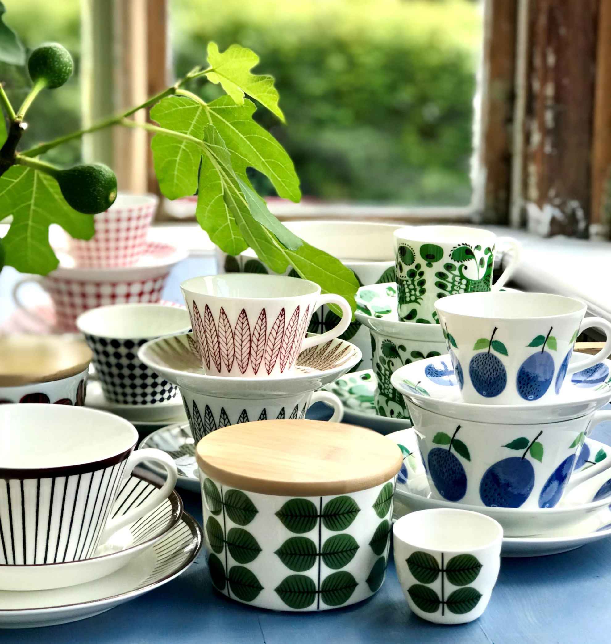Gros plan sur des tasses à café en porcelaine avec différents motifs sur une table et une brindille d'une plante verte.