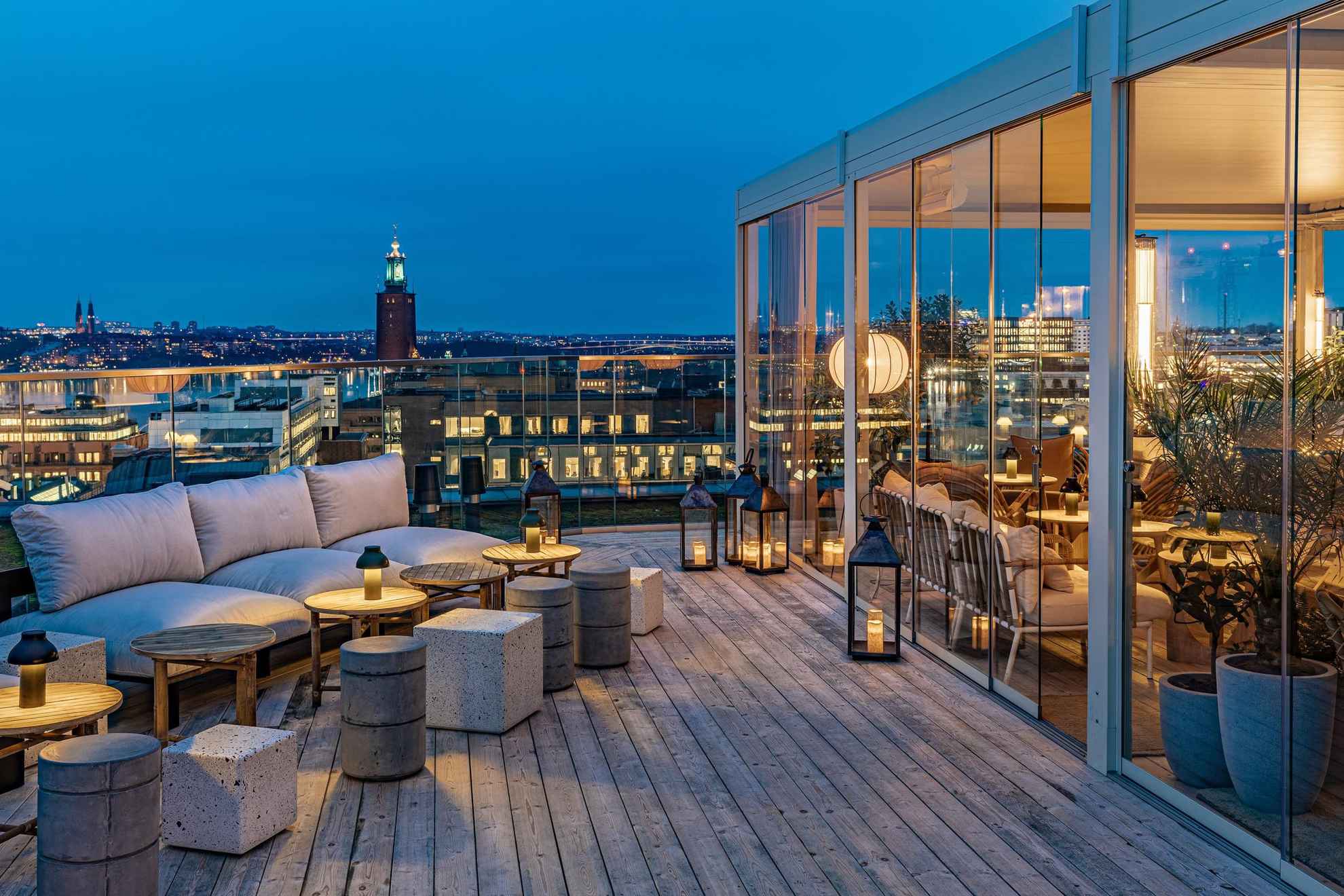 Un bar élégant sur un toit-terrasse avec vue sur Stockholm et l'hôtel de ville. La partie de la terrasse située sur la droite de la photo se trouve derrière un mur de verre.