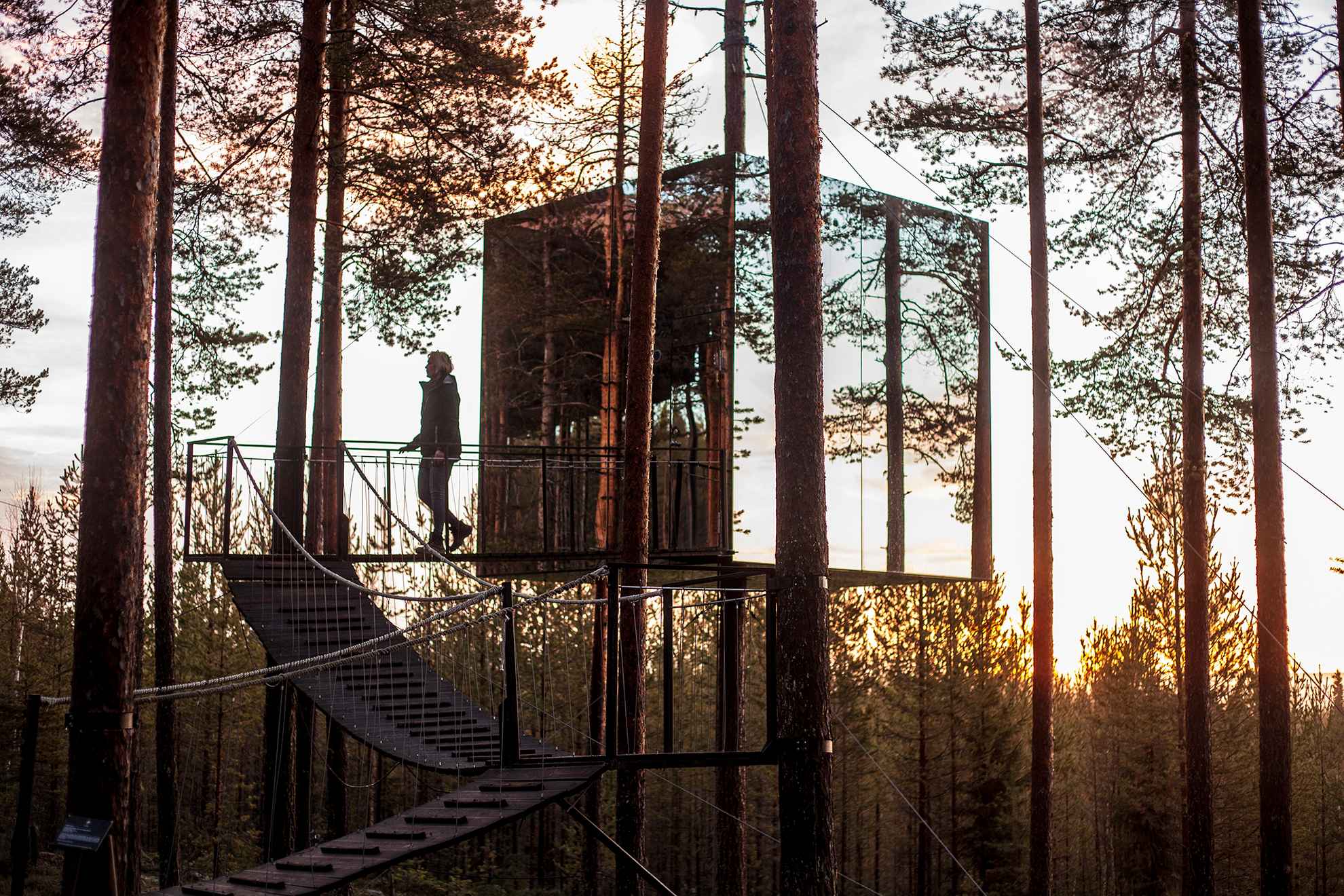 Une cabane dans les arbres en miroir, au coucher du soleil, en Laponie suédoise.