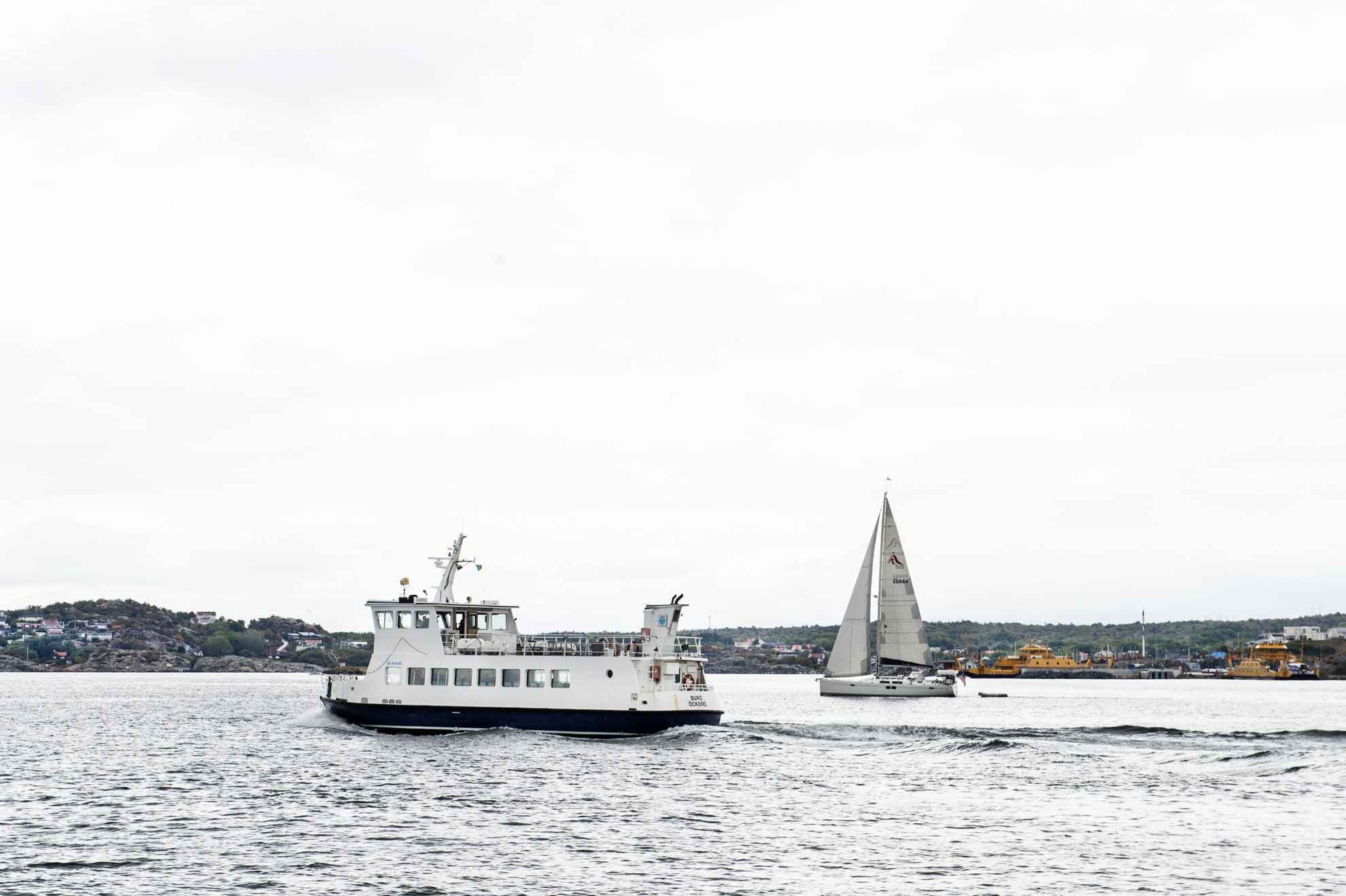 Un petit ferry et un bateau à voile sont sur l'eau et passent à côté d'une île au large de Göteborg.