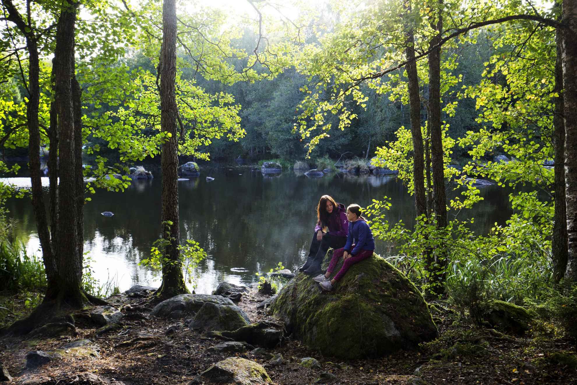 Deux filles sont assises sur un rocher, à côté d'un lac, dans la nature.