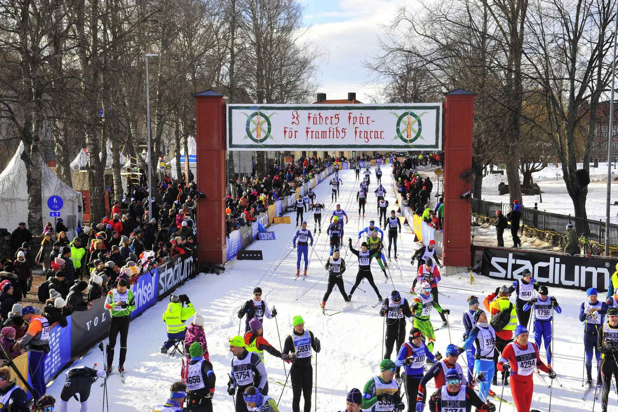 De nombreux skieurs passent la ligne d'arrivée de la Vasaloppet. Des publics acclament les sportifs de chaque côté de la piste.