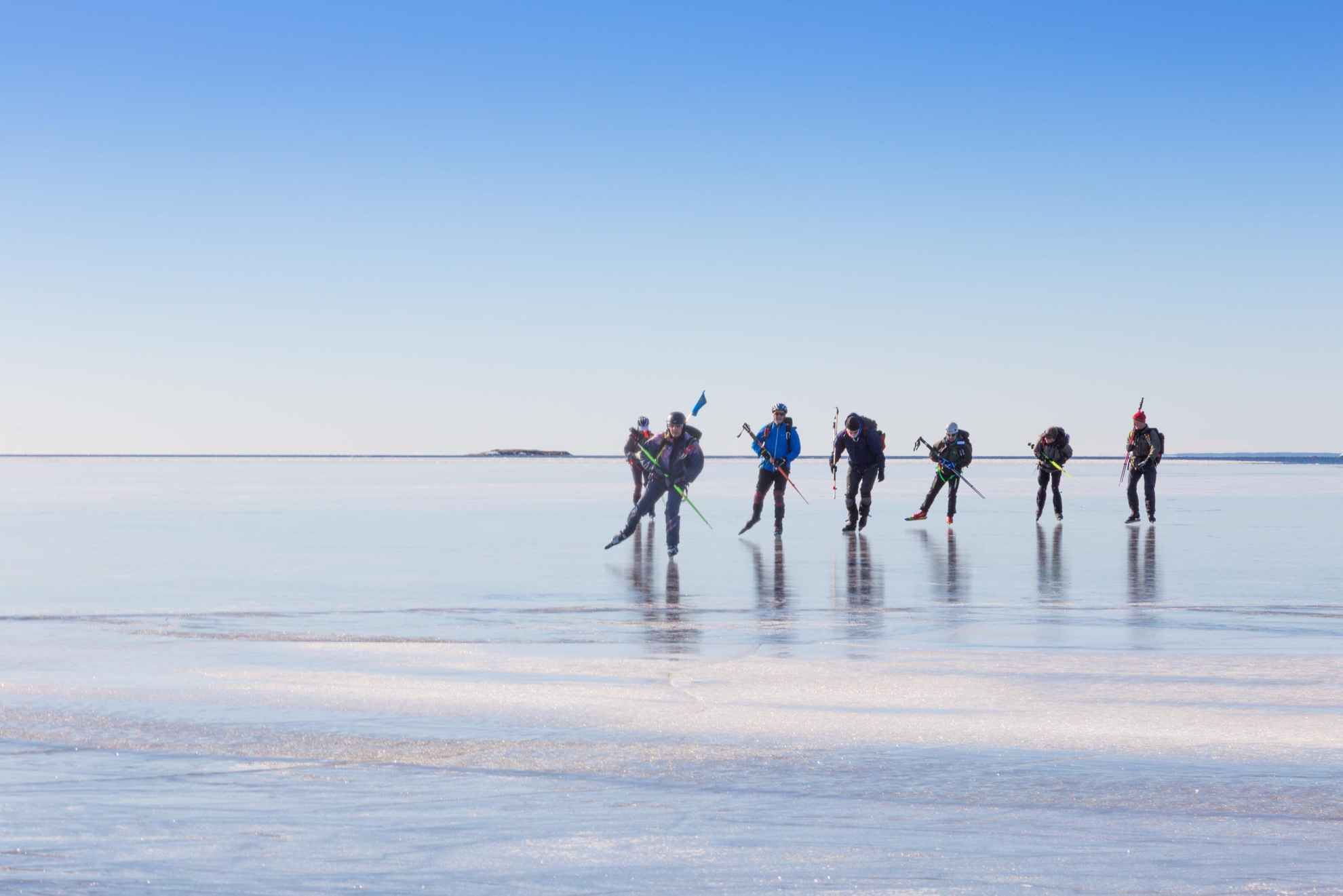 Sept personnes patinent sur de la glace lumineuse par une journée d'hiver ensoleillée.