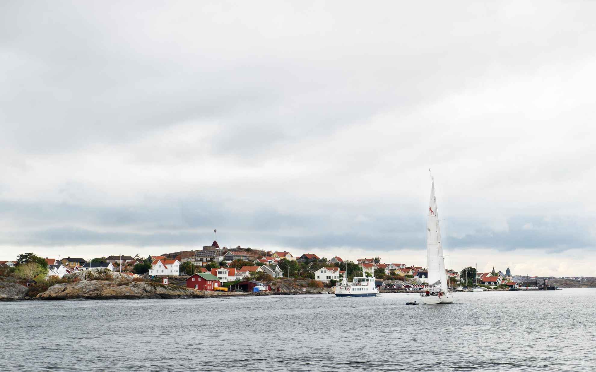 Un petit ferry et un voilier en mer, passant au large d'une île avec de nombreuses maisons à l'extérieur de Göteborg.