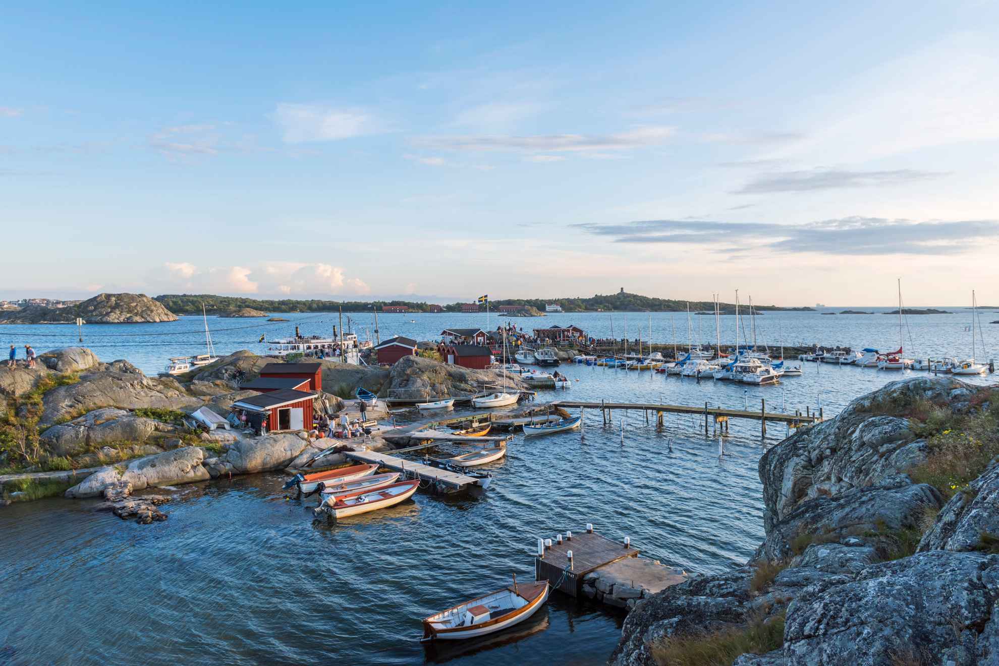 L'île de Brännö, dans l'archipel de Göteborg, avec des bateaux, des falaises rocheuses et des jetées, des petites maisons rouges, un drapeau suédois et des gens au soleil.