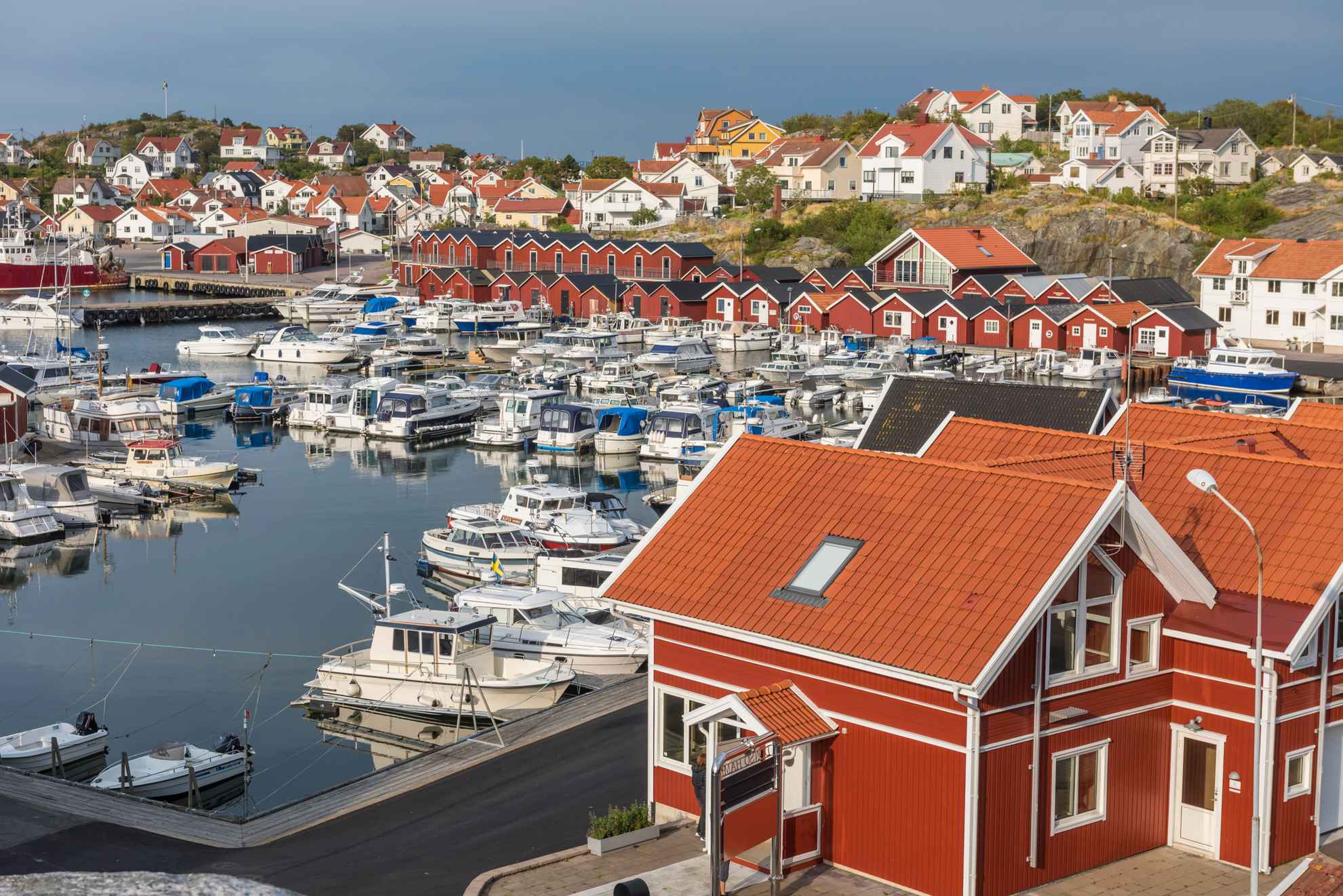 Un port avec des bateaux, des cabanes de pêcheurs rouges et des maisons blanches.