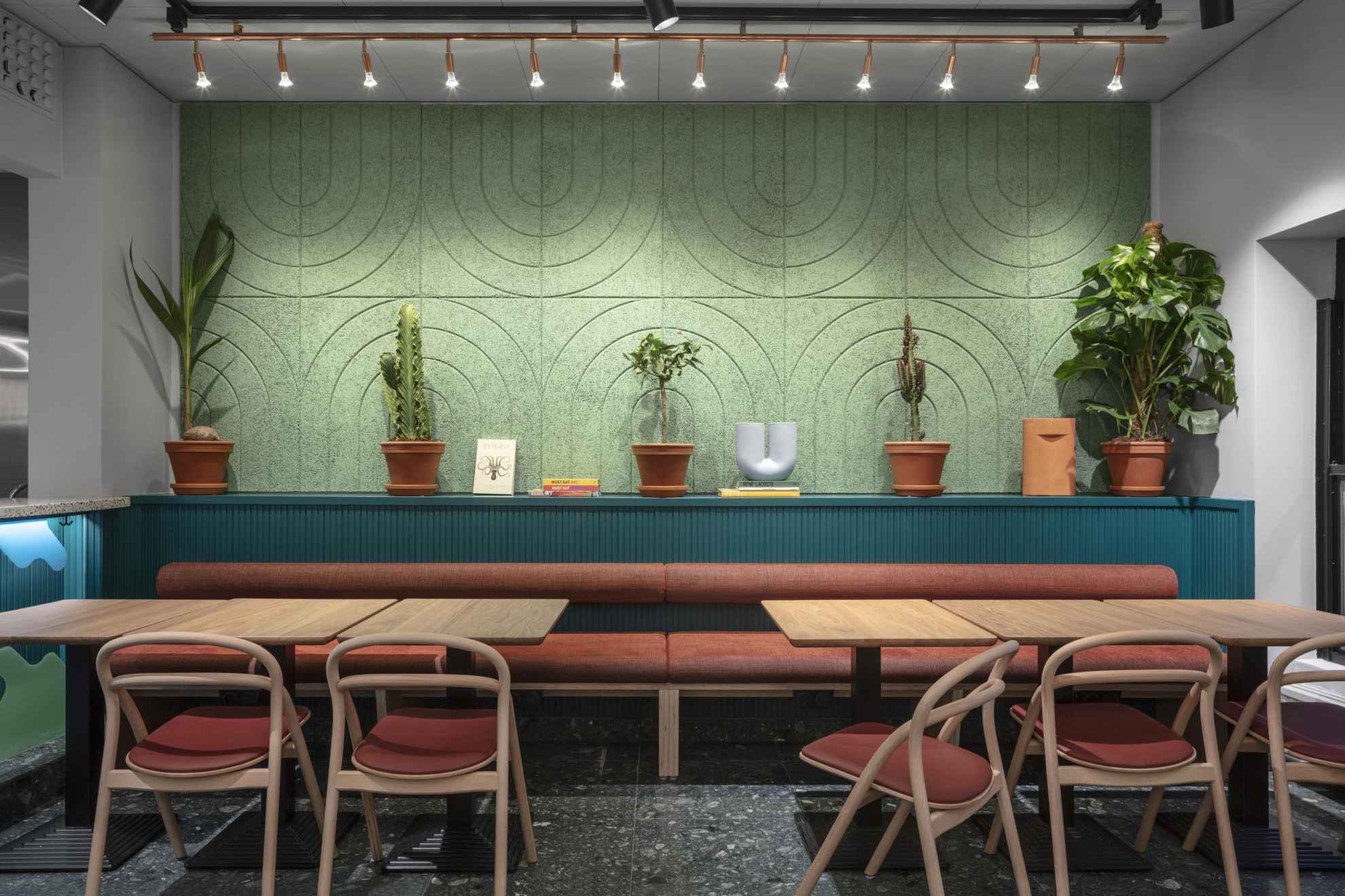 Un coin salon. Quelques plantes décorent le mur vert et bleu derrière la table.