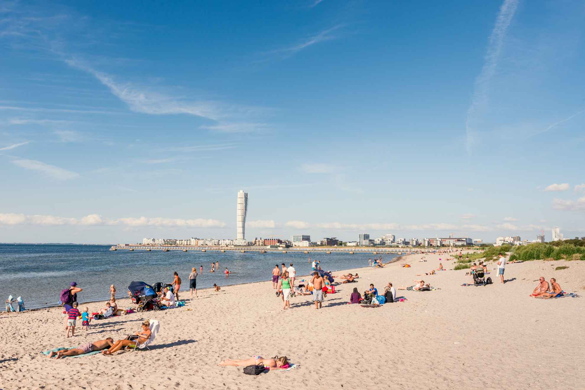 Des gens s'amusent sur une plage de Malmö. À l'horizon, on peut apercevoir le bâtiment "Turning Torso".
