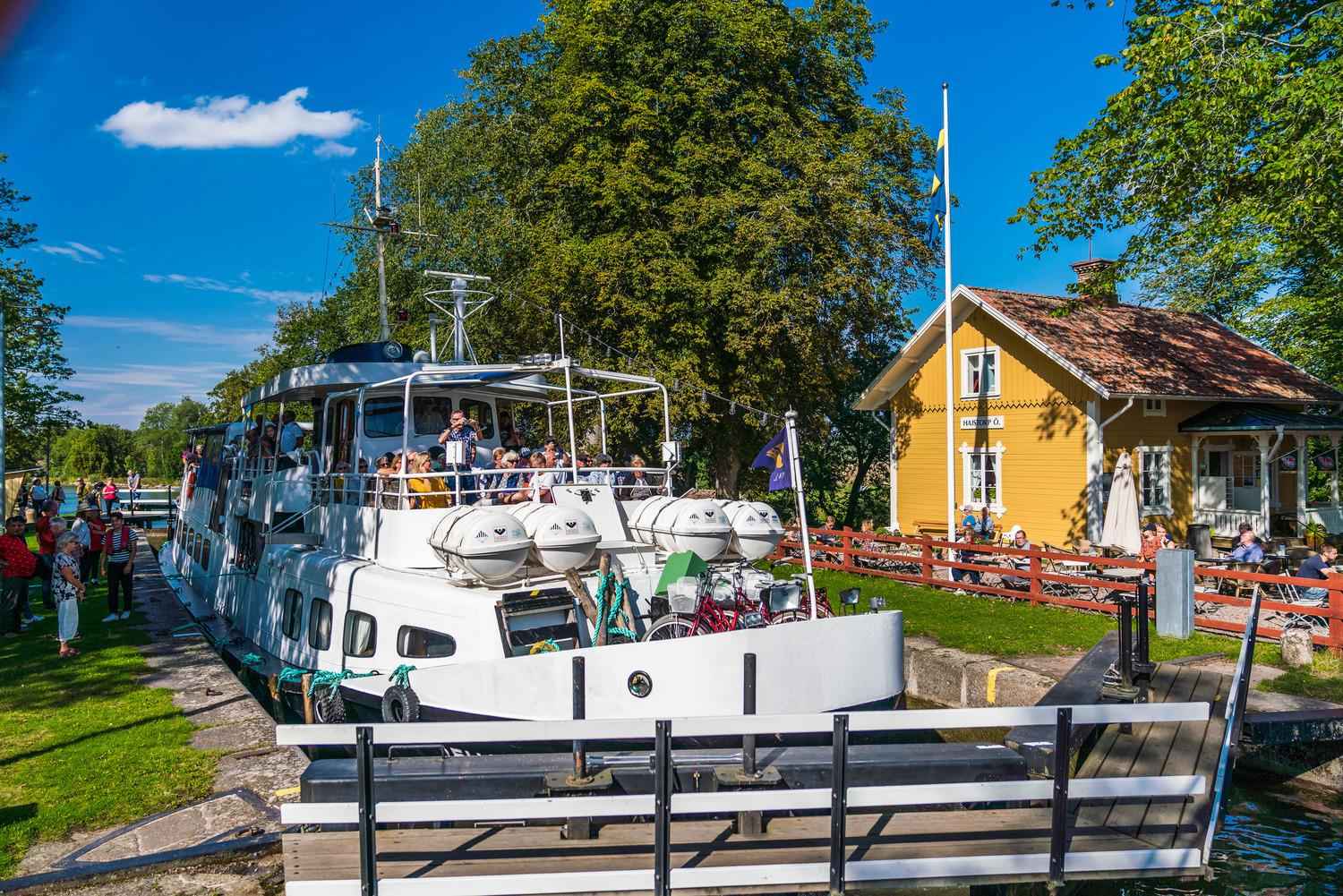 Une grand bateau blanc devant la maison en bois jaune du Hajstorp Slusscafé & Vandrarhem