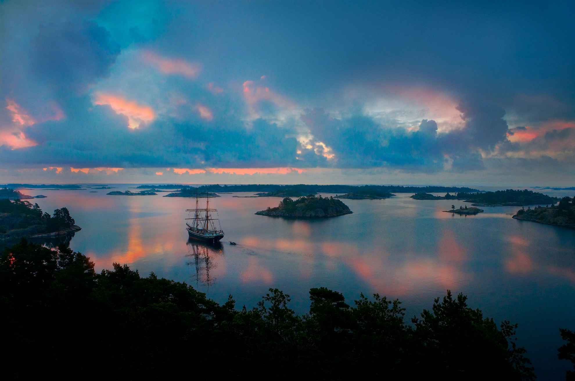 Un voilier se trouve dans l'eau entre les îles de Gryt dans l'archipel d'Östgöta. C'est le soir, l'eau est calme et reflète le ciel et les environs.
