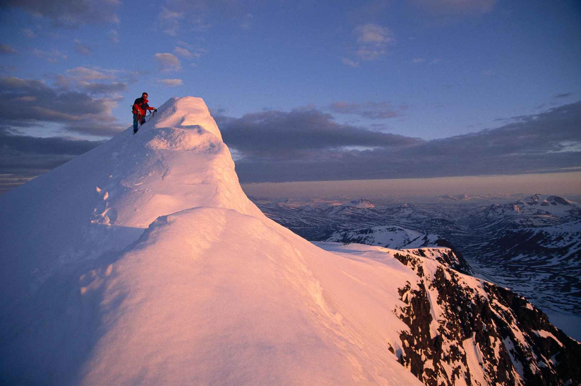Une personne se tient debout au sommet d'une montagne enneigée.