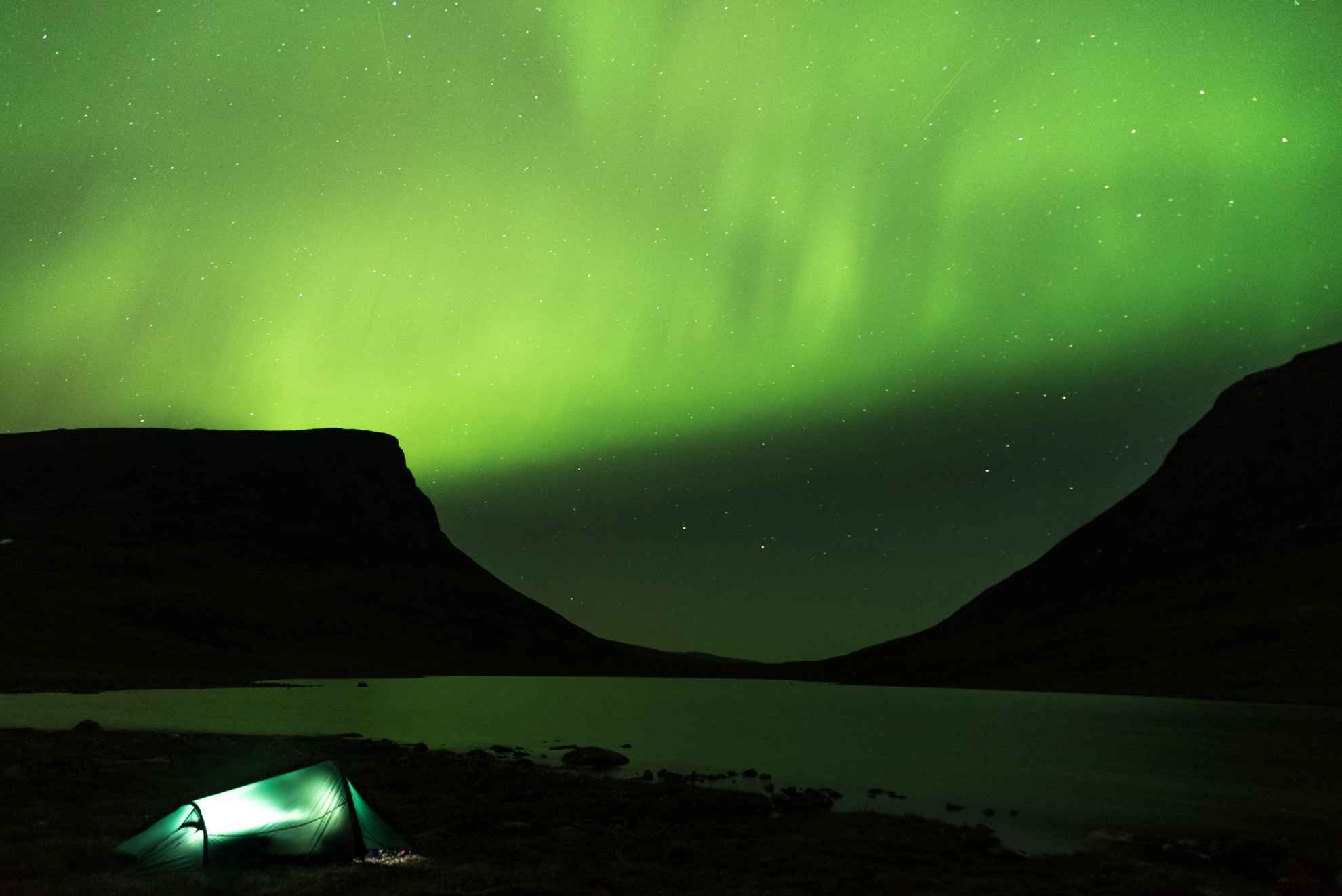 Des aurores boréales dansent au-dessus des montagnes Lapporten à Abisko. Au bord du lac Torne, une tente dressée est éclairée de l'intérieur.