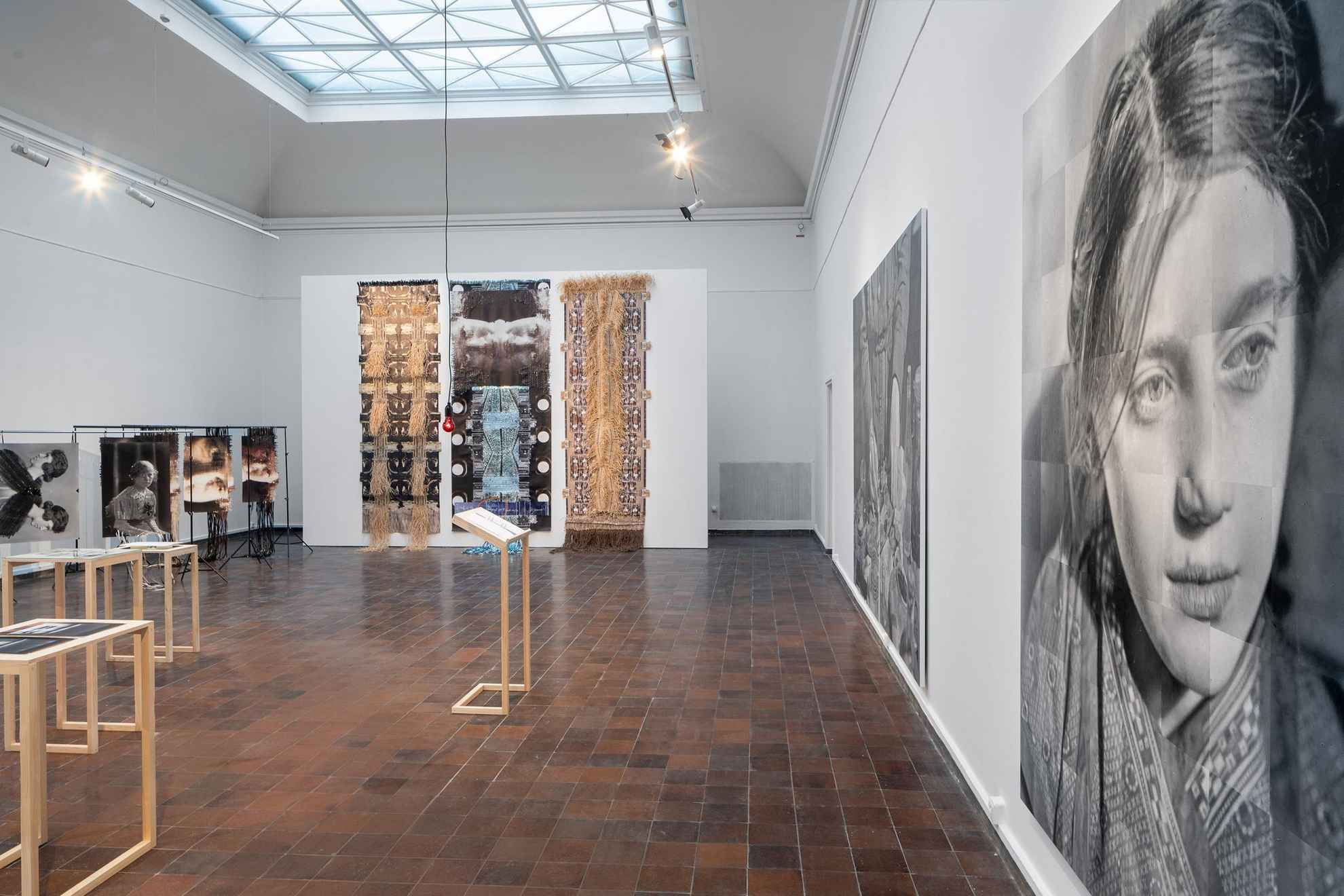 Installation dans une exposition. Une grande image en noir et blanc d'une femme à l'avant et une grande œuvre d'art avec des photographies tressées dans de nouvelles structures, à l'arrière-plan.