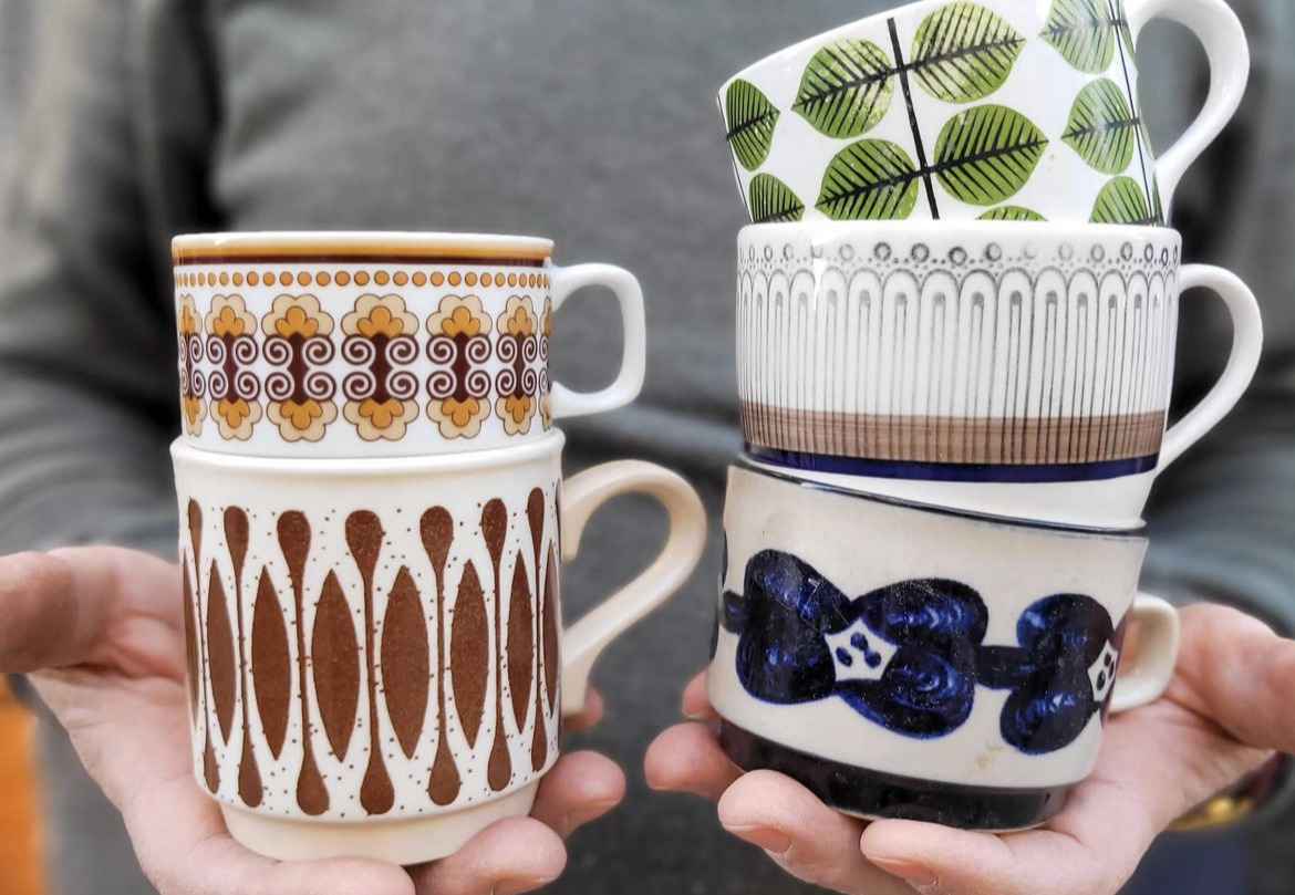 Deux mains tiennent cinq mugs d'occasion aux motifs différents.