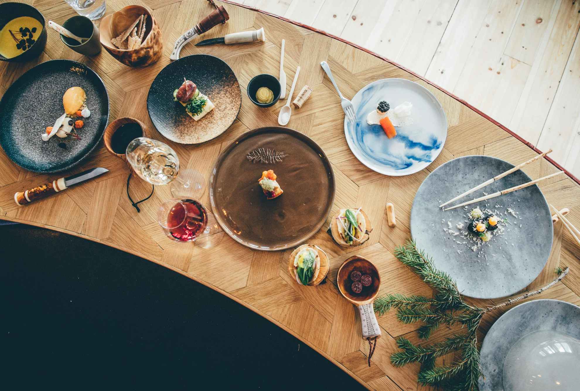 Une table en bois avec de la nourriture, des assiettes, des verres à vin et des couverts.
