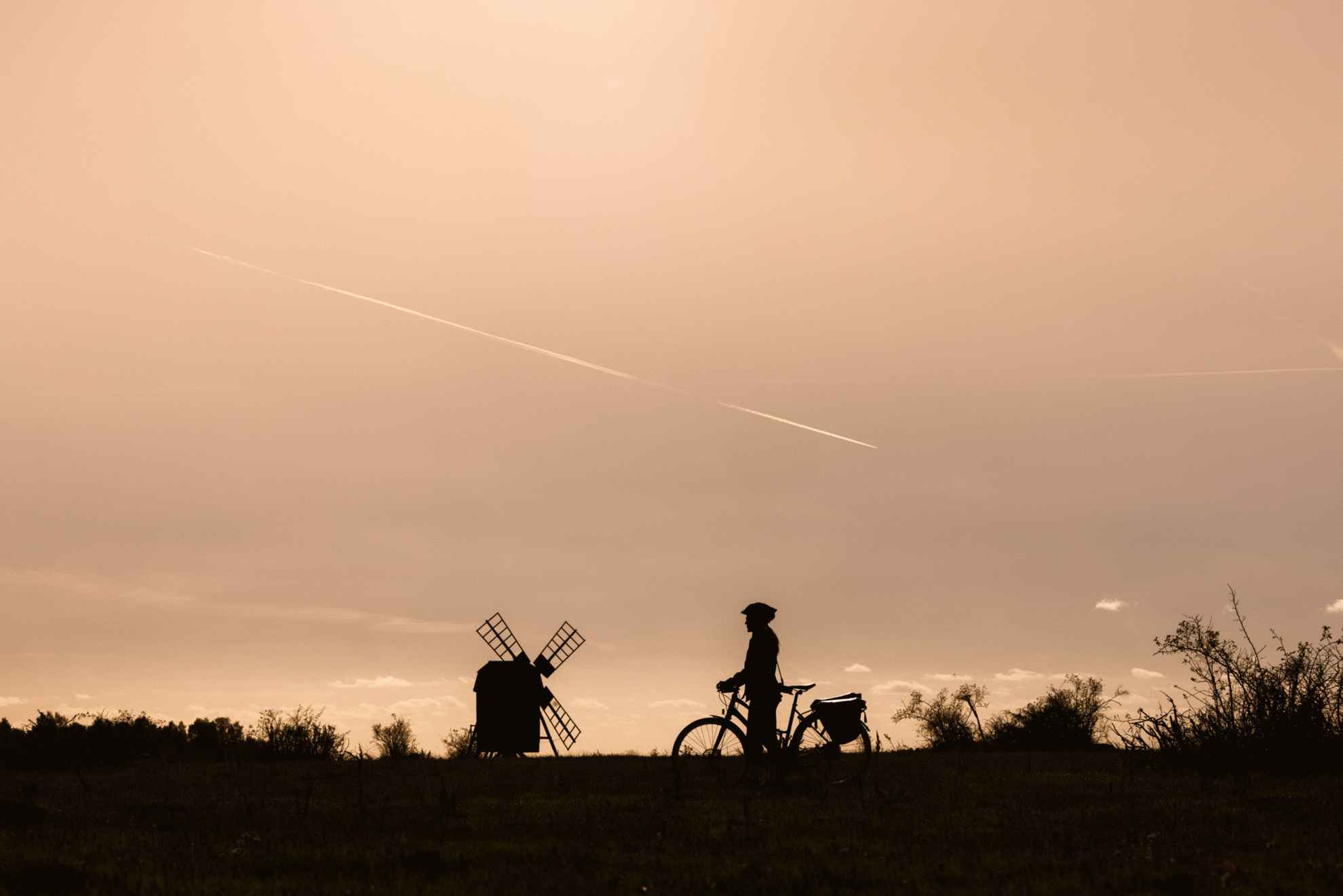 On voit sur la photo la silhouette d'un cycliste au crépuscule avec un moulin à vent en arrière-plan