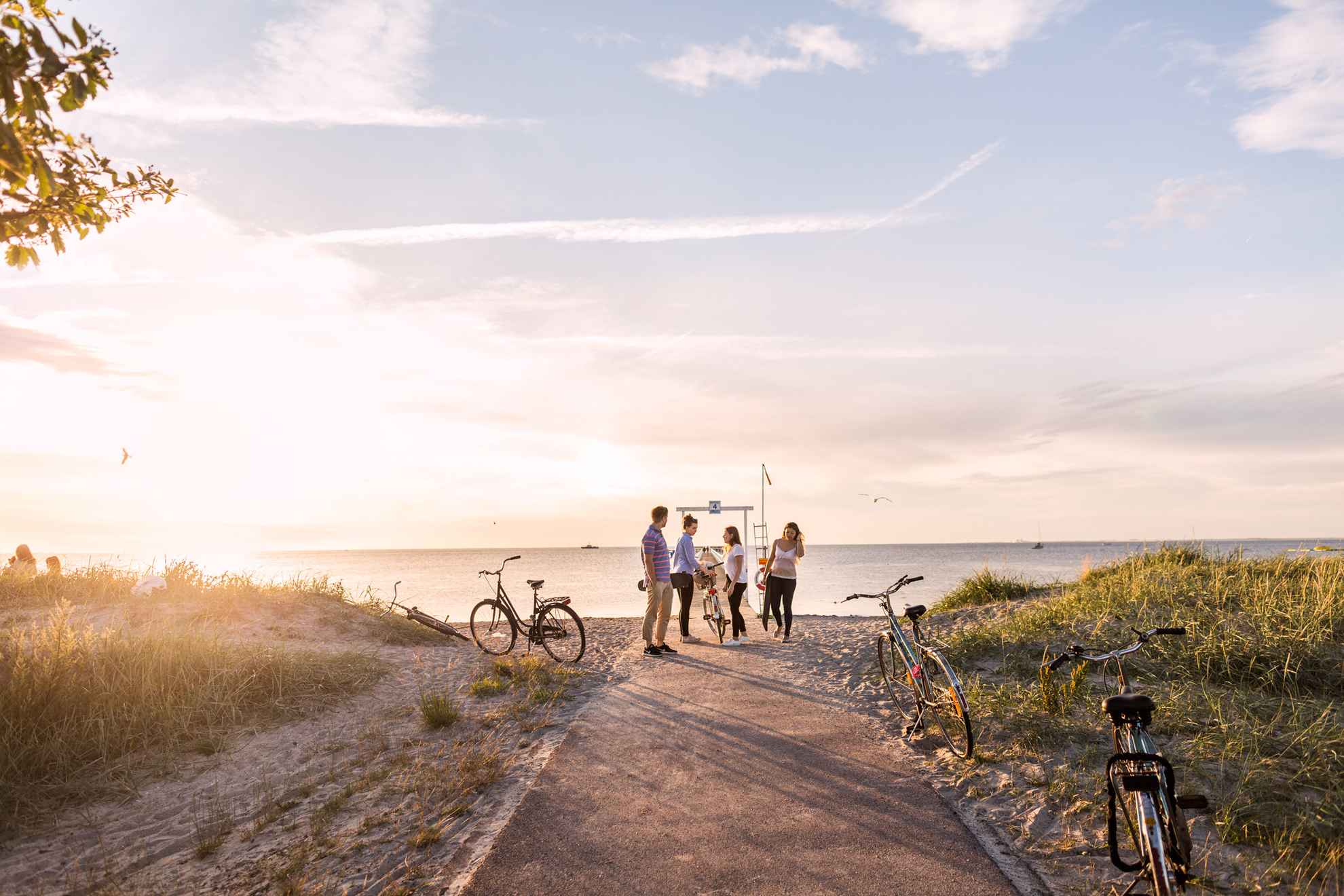 Coucher de soleil sur la plage de Ribersborg. Un homme et trois femmes sont près de la jetée de la plage. Des vélos sont garés le long du chemin menant à la plage.