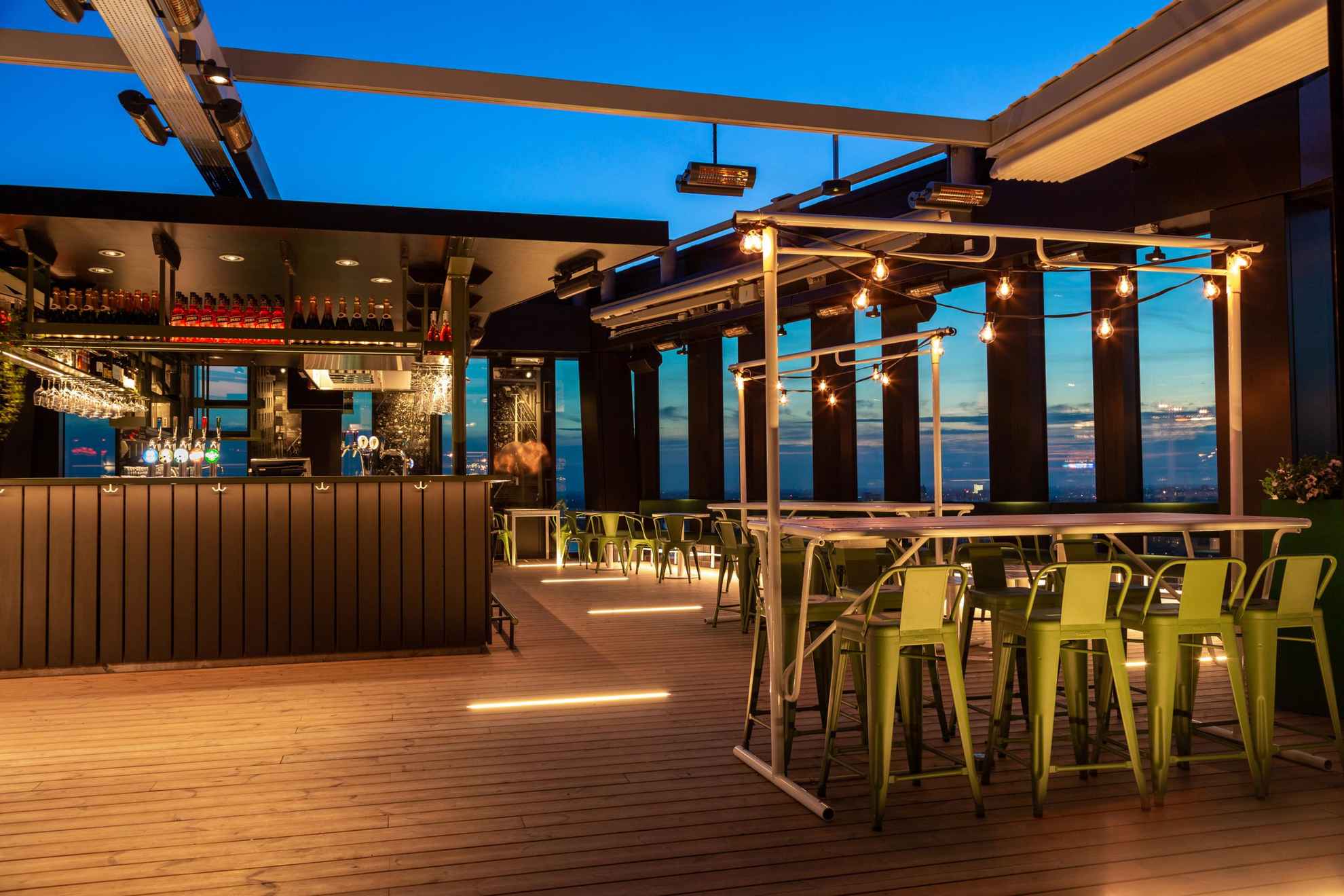 Un bar rooftop avec des sièges et des tables posées sur un parquet en bois.