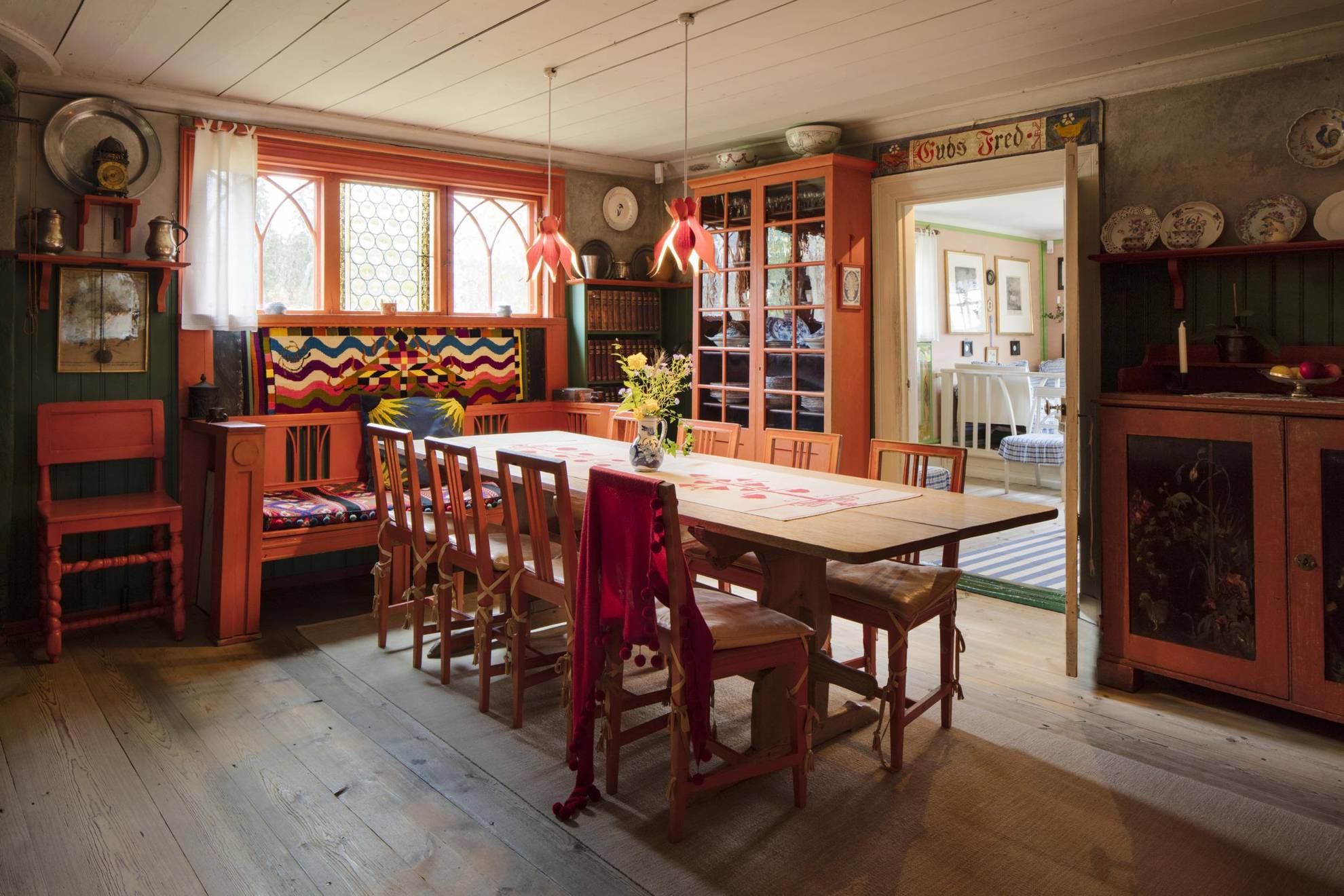 Design d'intérieur suédois chez Lilla Hyttnäs comprenant une grande table à manger, des meubles en bois rouge et des objets en porcelaine sur certains murs.