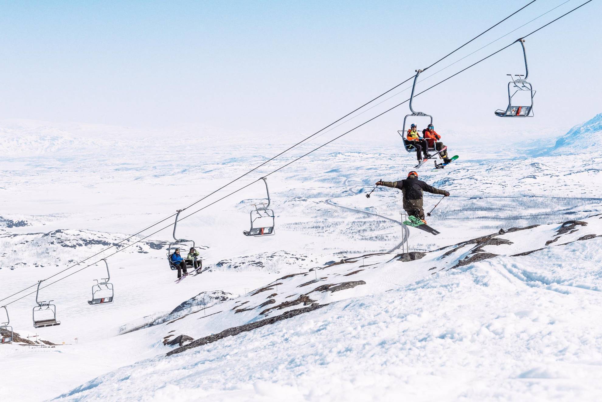 Des gens assis sur un remonte-pente regardant une personne sautant avec des skis.