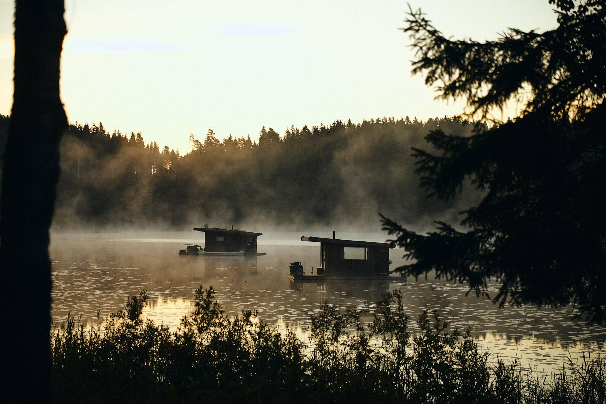 Deux péniches en bois sur un lac recouvert de brume.