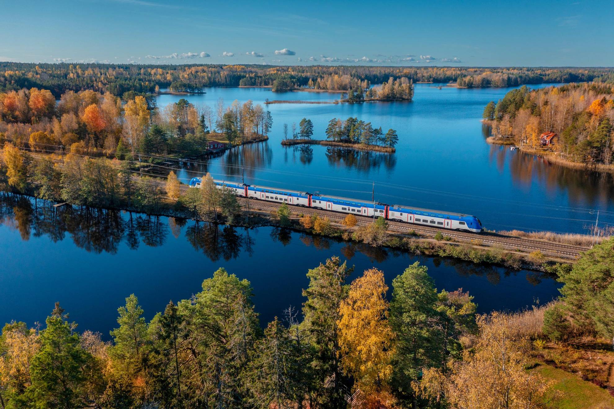 Vue aérienne d'un train traversant un paysage automnal composé de forêts et lacs.