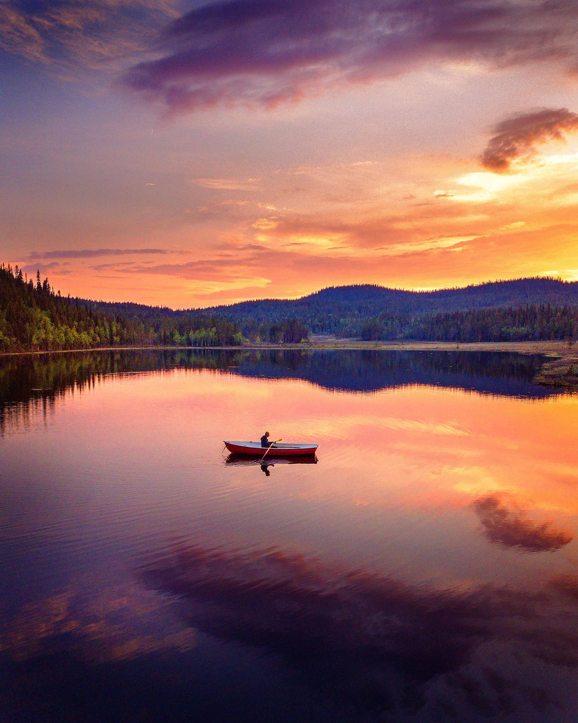 Une personne est en train de ramer dans une barque sur un lac de Laponie suédoise reflétant la lumière du soleil de minuit.