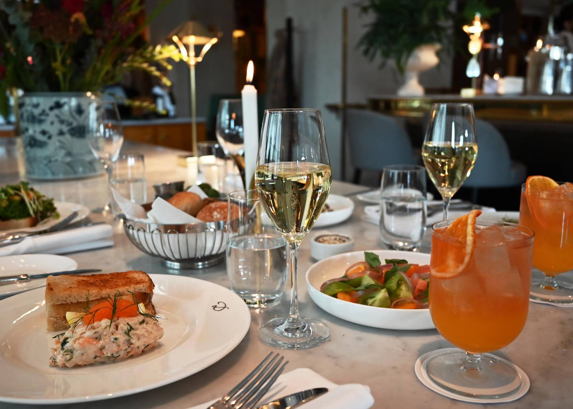 Une table est dressée avec des couverts, des assiettes remplies de nourriture, des verres d'eau et des verres à pied contenant du vin blanc.
