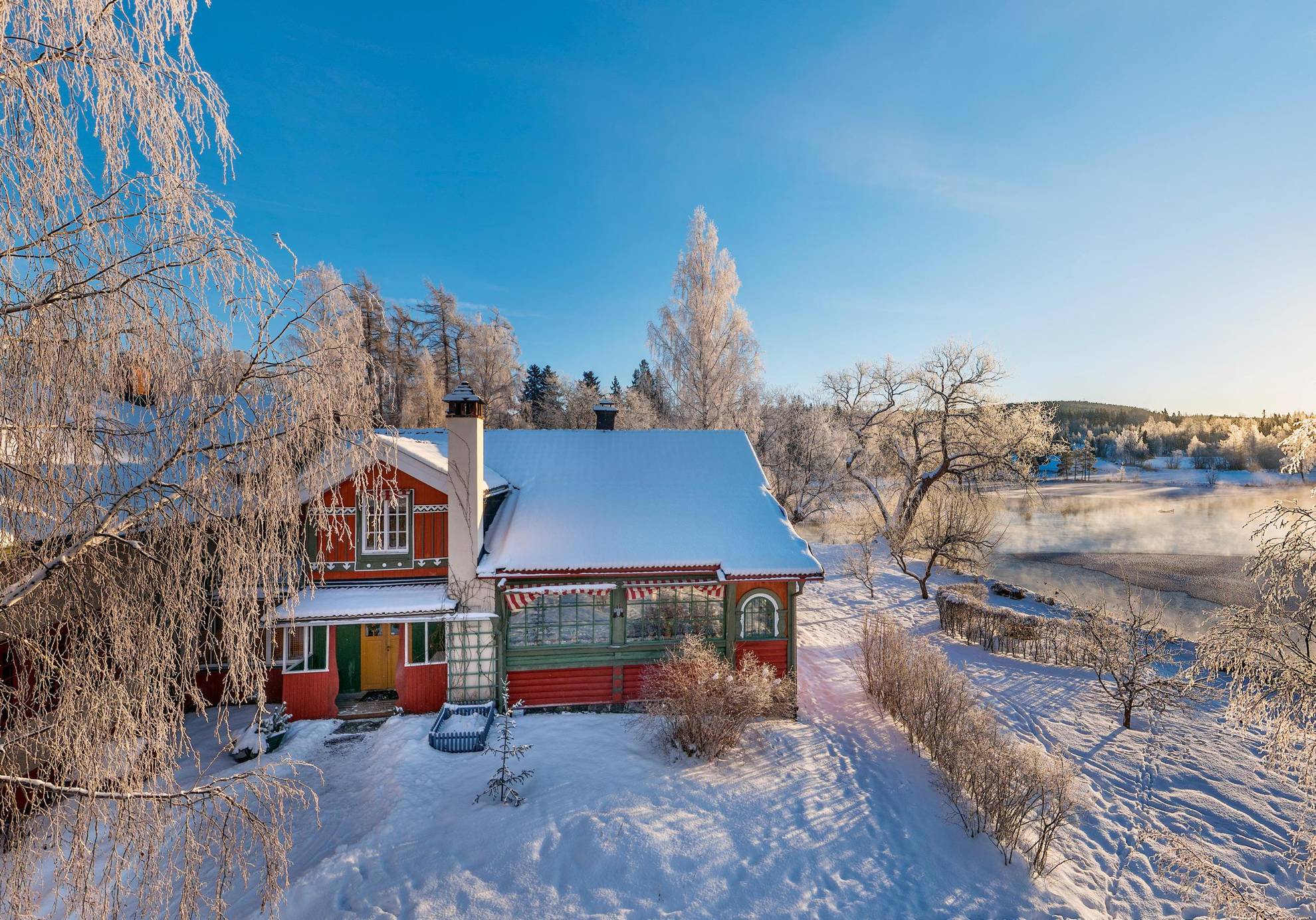 Une maison au bord de l'eau dans un paysage hivernal glacial et enneigé. On voit un lac en arrière-plan.