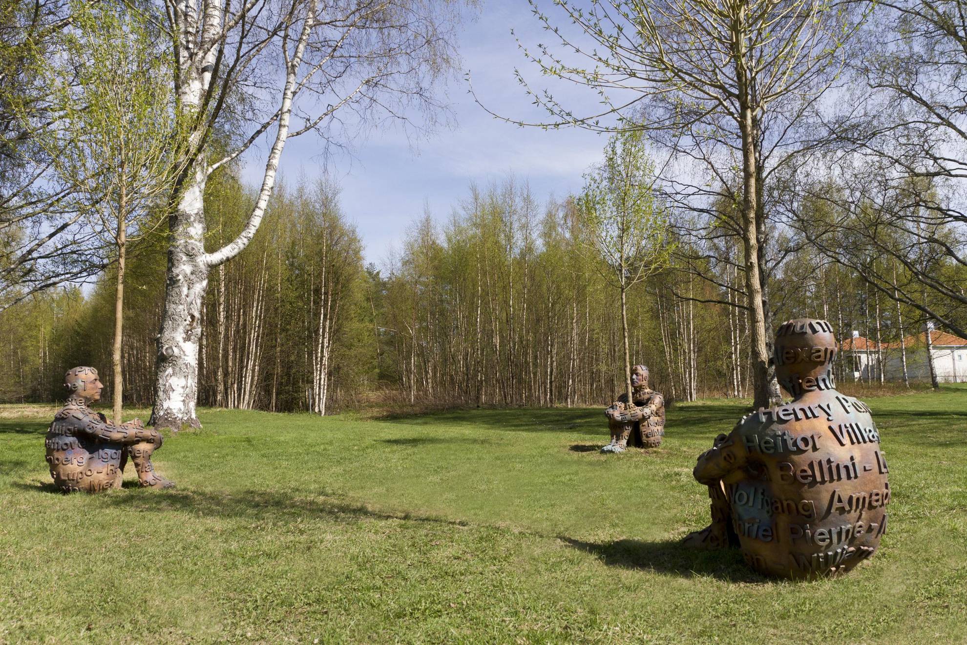 On voit trois sculptures en forme d'humains assis étreignant chacune un arbre au parc de sculptures d'Umedalen.