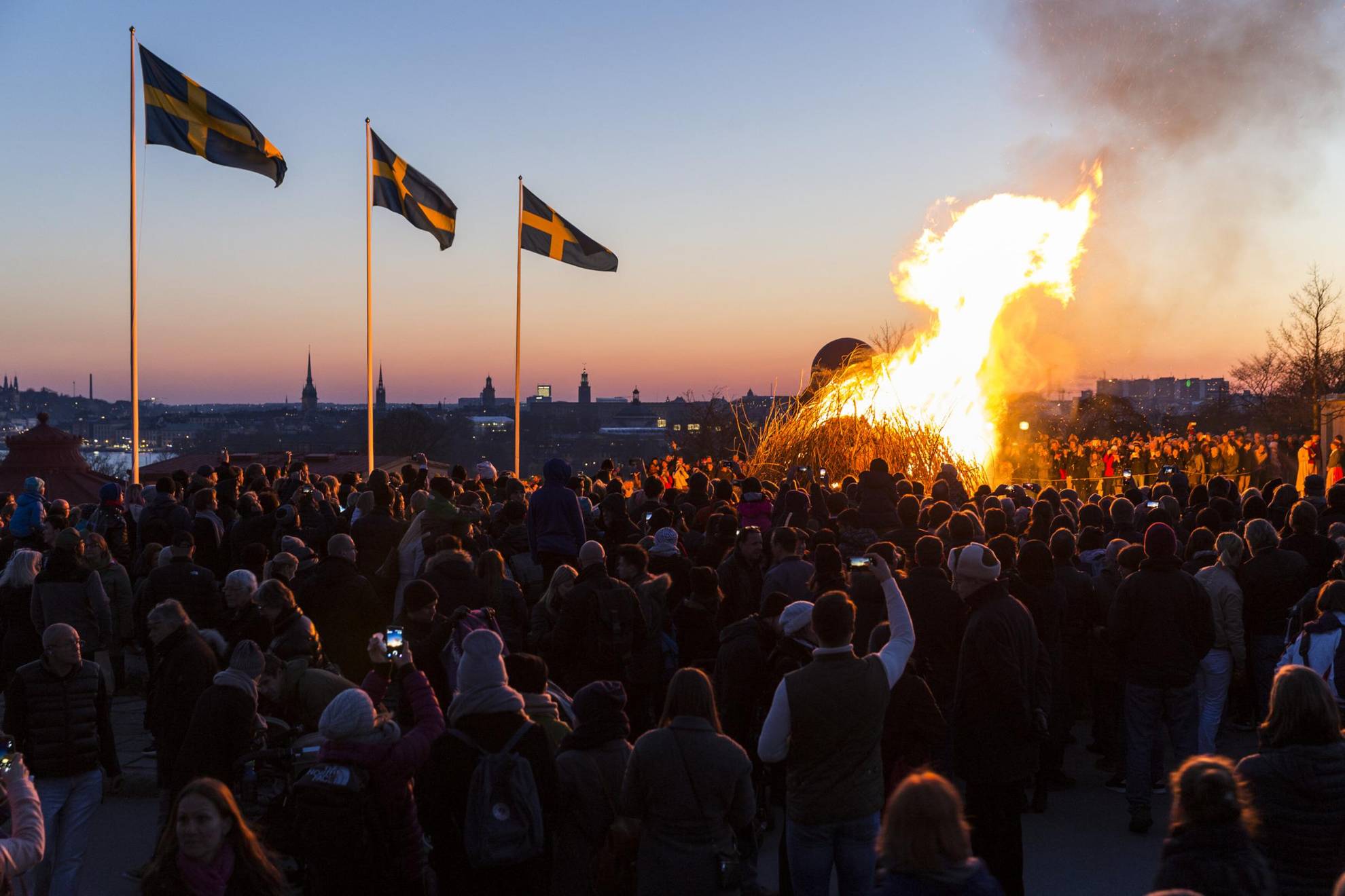 Des gens se sont rassemblés autour d'un feu de joie pour célébrer la nuit de Walpurgis. Trois drapeaux suédois flottent au vent.