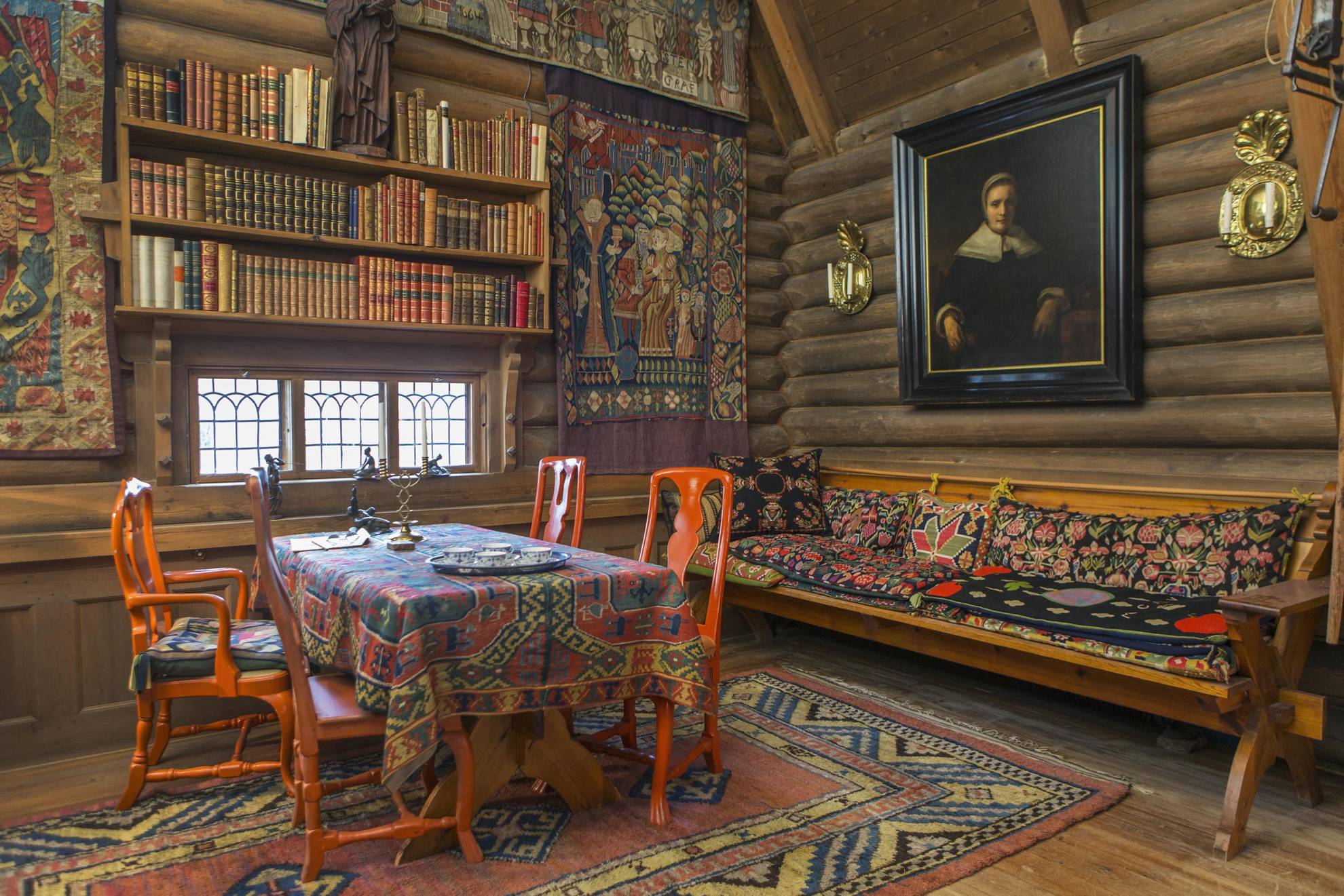 La salle à manger colorée d'Anders Zorn, avec des tapisseries, des chaises rouge vif autour d'une table avec un tissu tissé, une étagère et un canapé en bois.