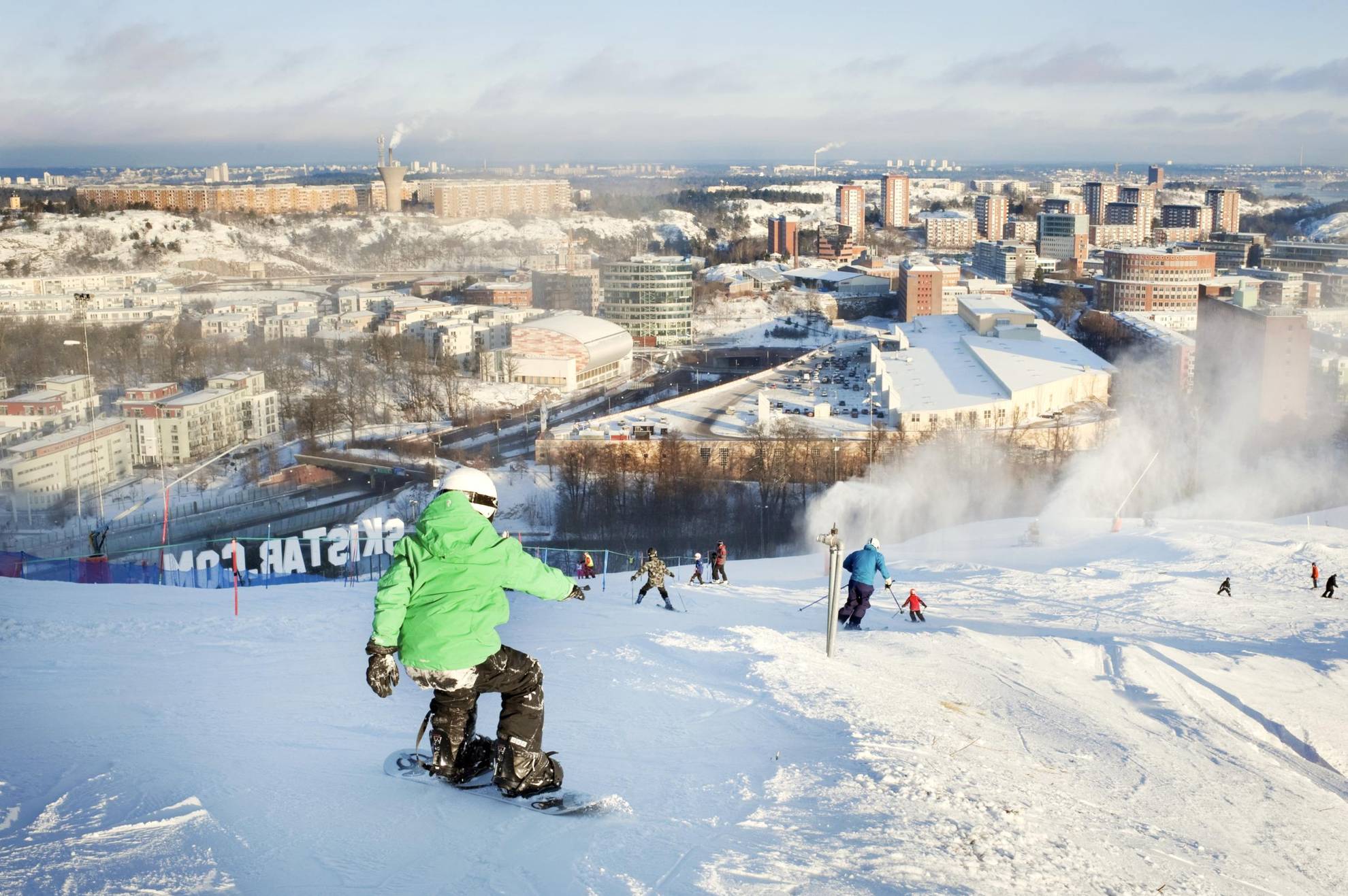 Des personnes en train de descendre des pistes de Hammarbybacken en snowboard en regardant la vue sur Stockholm