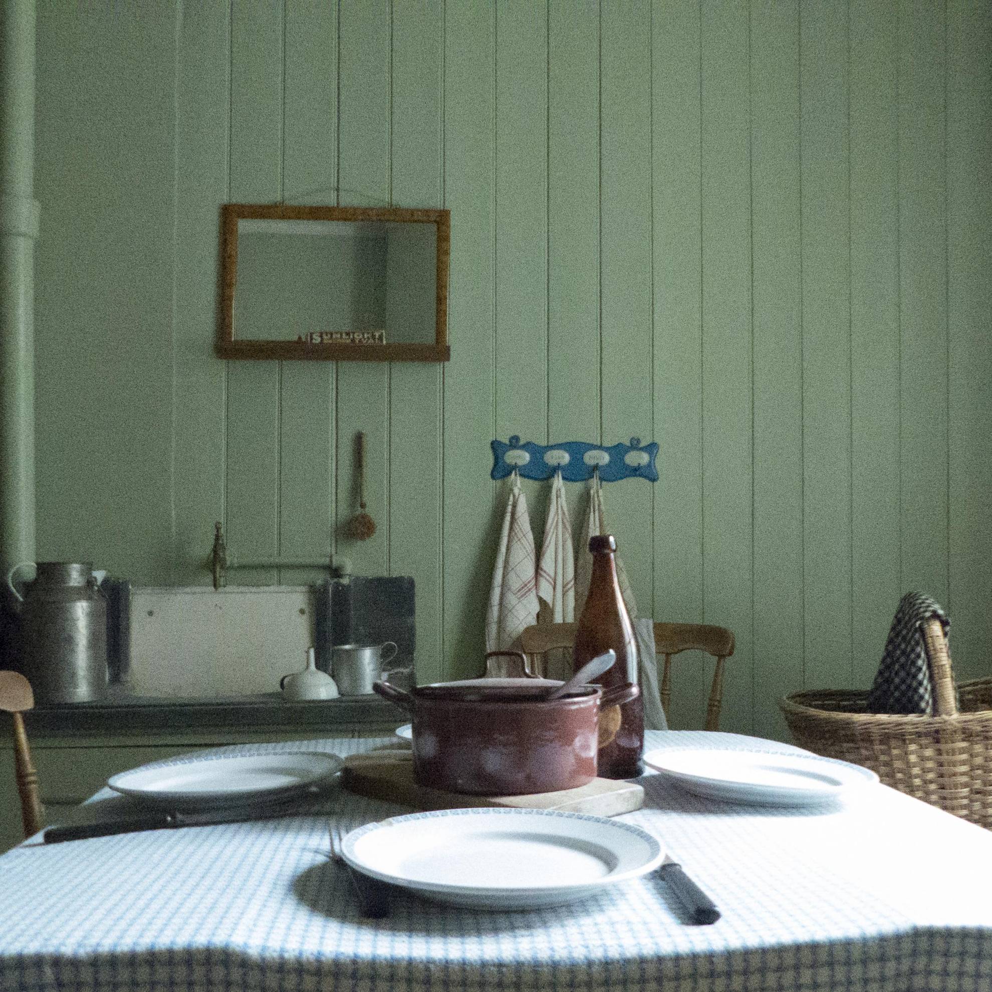 À l'intérieur d'une maison ouvrière dans la première banlieue de Göteborg aux XIXe et XXe siècles. Une table dressée avec un pot en fer au milieu. Un miroir est accroché sur un mur en bois vert.
