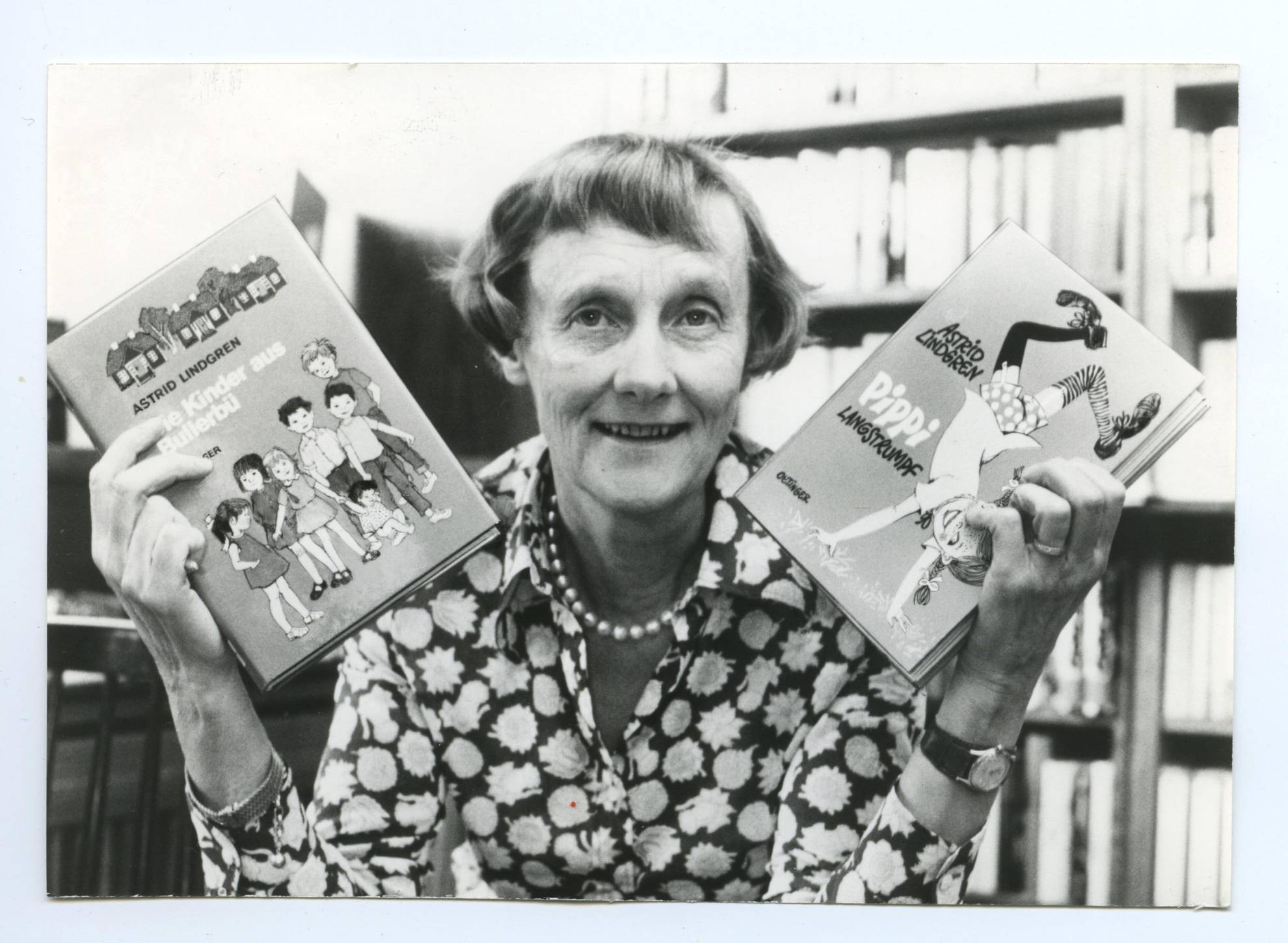 Un portrait en noir et blanc de l'auteur Astrid Lindgren tenant son livre de Fifi Brindacier dans un main et un livre "The Children of Noisy Village" dans l'autre main.