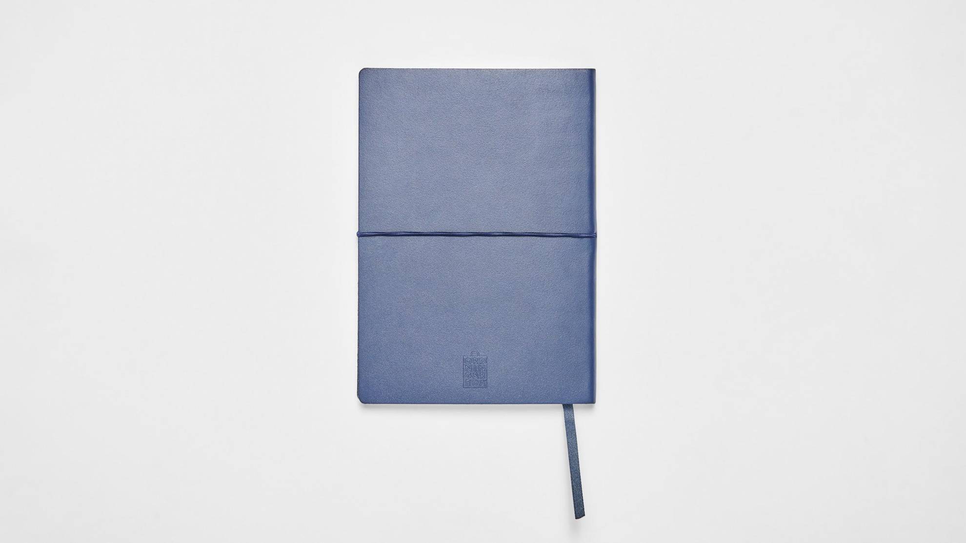 Un cahier à la couverture rigide bleue foncée est posé sur une surface blanche.