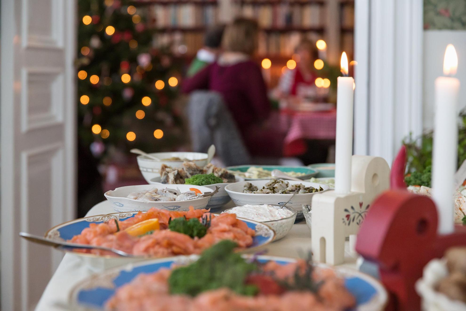 Ein gut gedeckter Tisch voll schwedischer Köstlichkeiten. Im Hintergrund steht ein beleuchteter Tannenbaum.