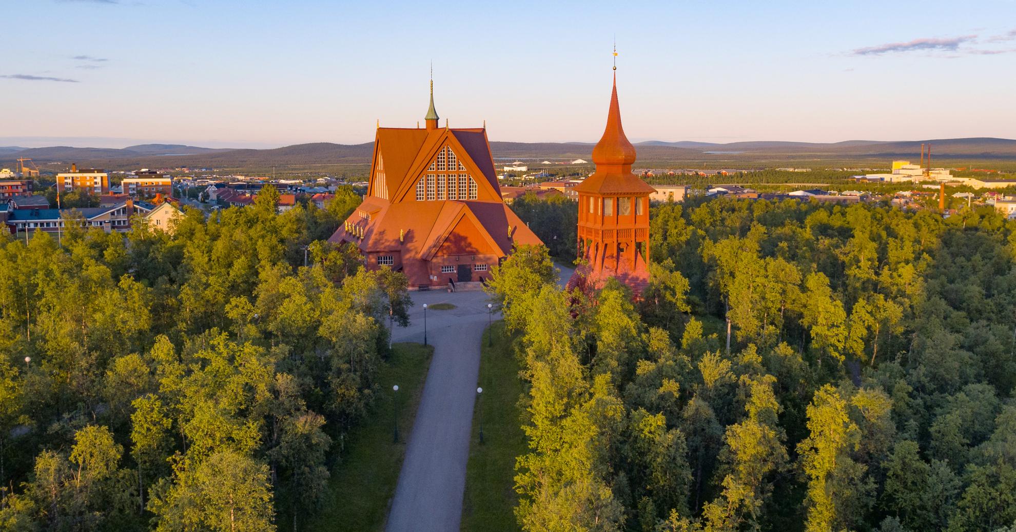 Le bâtiment rouge de l'église de Kiruna est entouré de verdure.