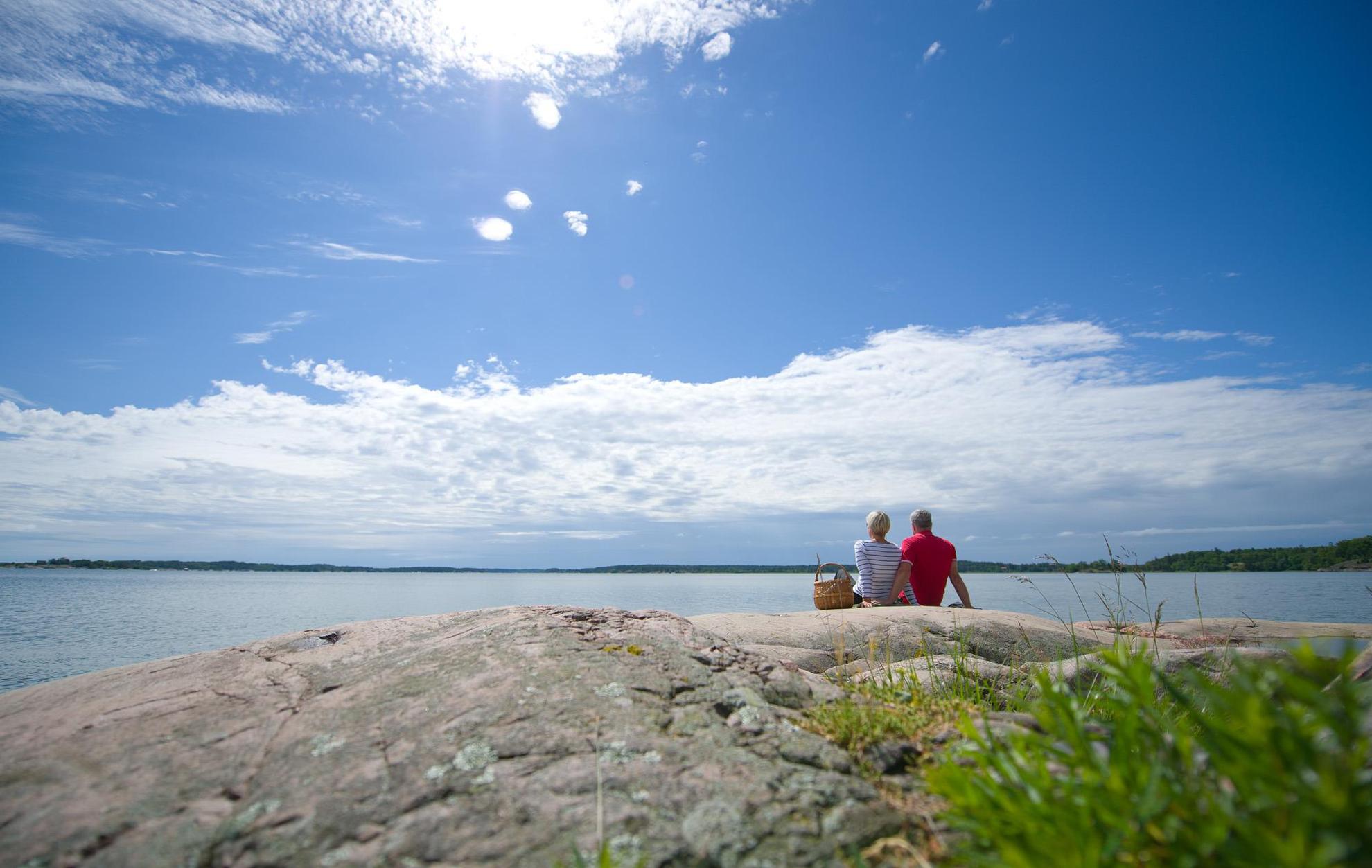 Un couple avec un panier de pique-nique assis côte à côte sur un rocher au bord de la mer.