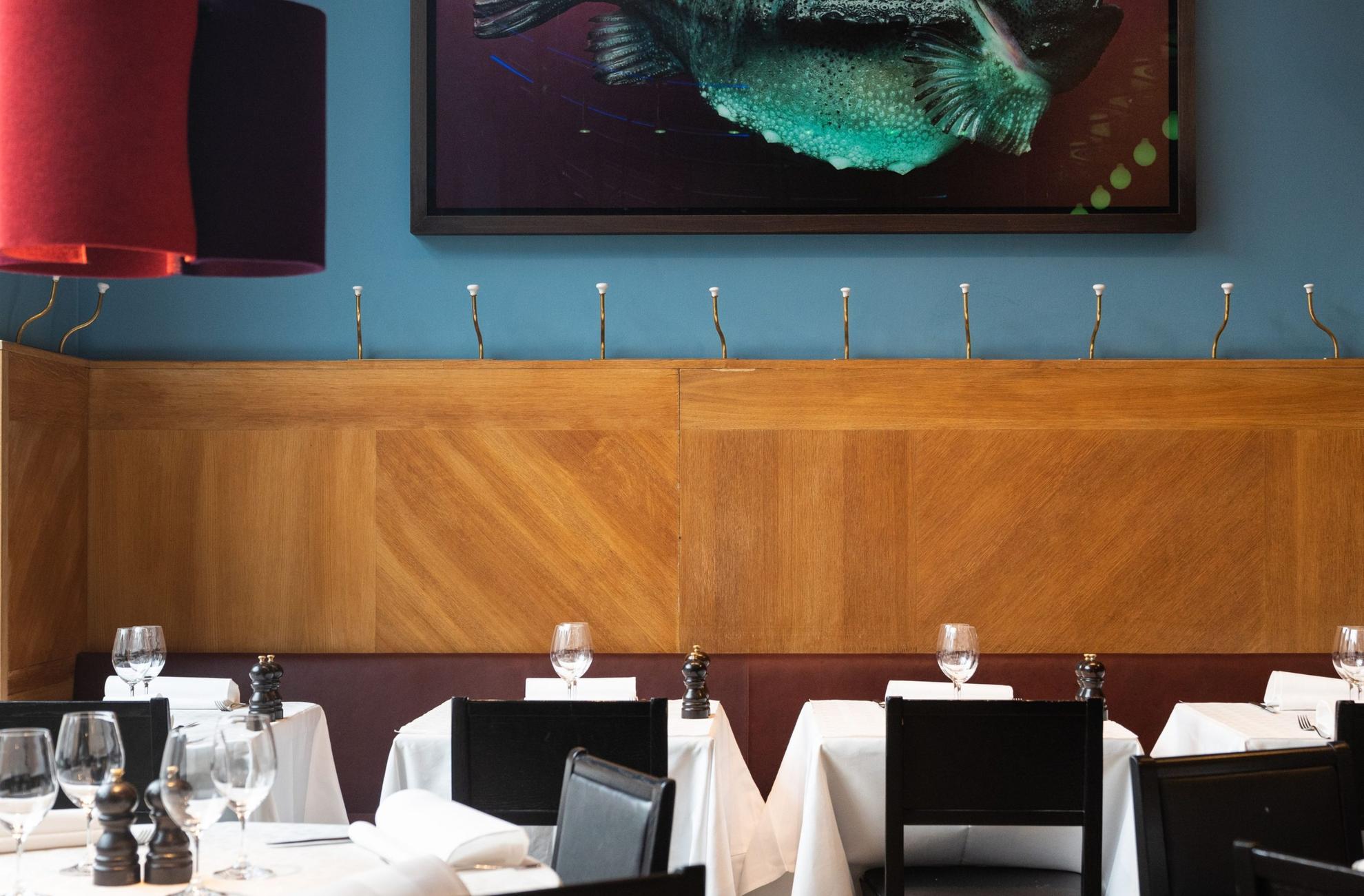 À Sturehof, les tables sont dressées avec des nappes blanches entourées de chaises noires. des planches en bois décorent un mur bleu clair.