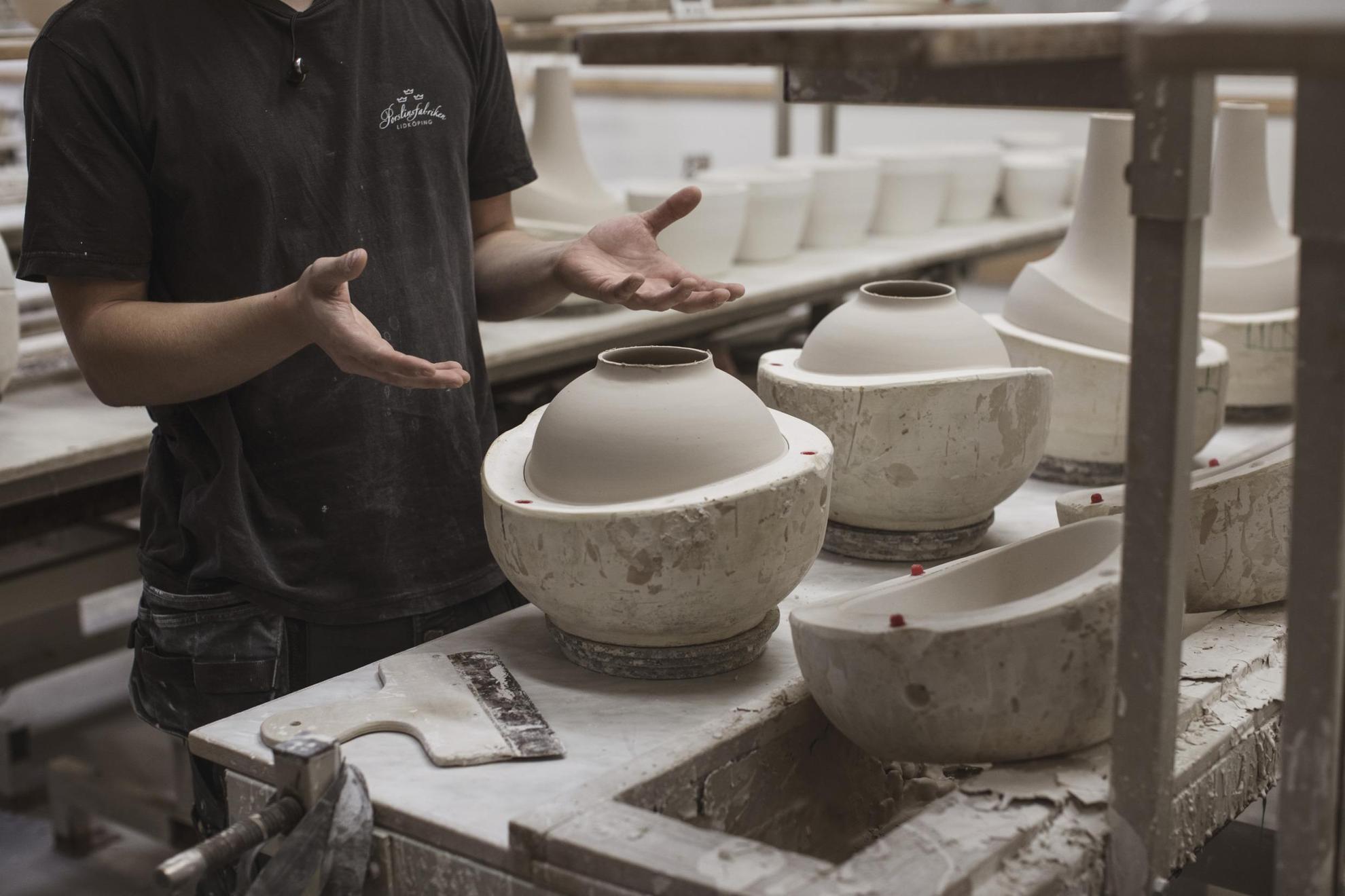 Quelqu'un montre plusieurs vases en céramique en cours de fabrication, dans un décor d'usine.