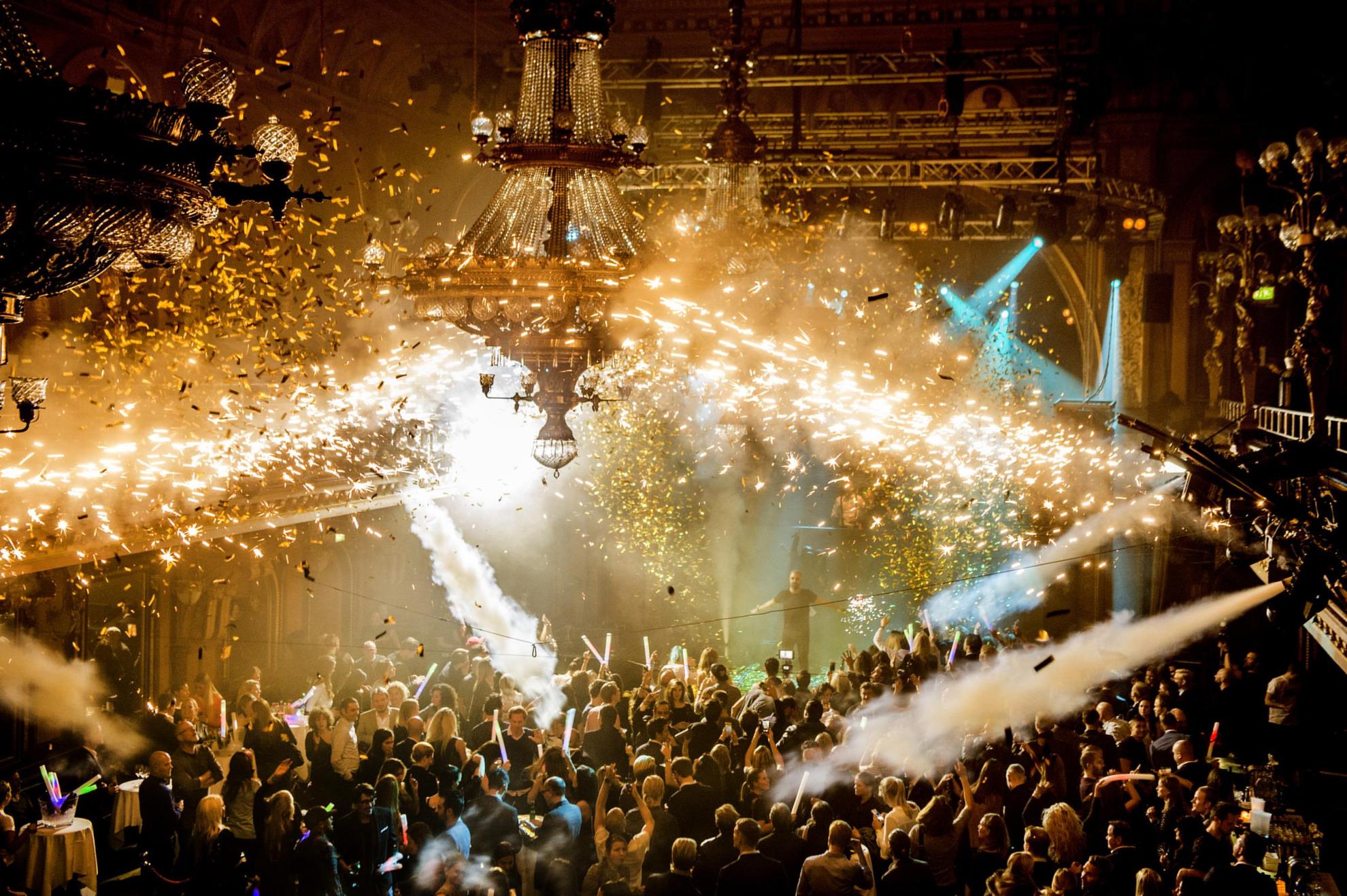 La boîte de nuit de Berns remplie de personnes en train de danser. Des canons soufflent de la fumée et des confettis au-dessus de la foule.