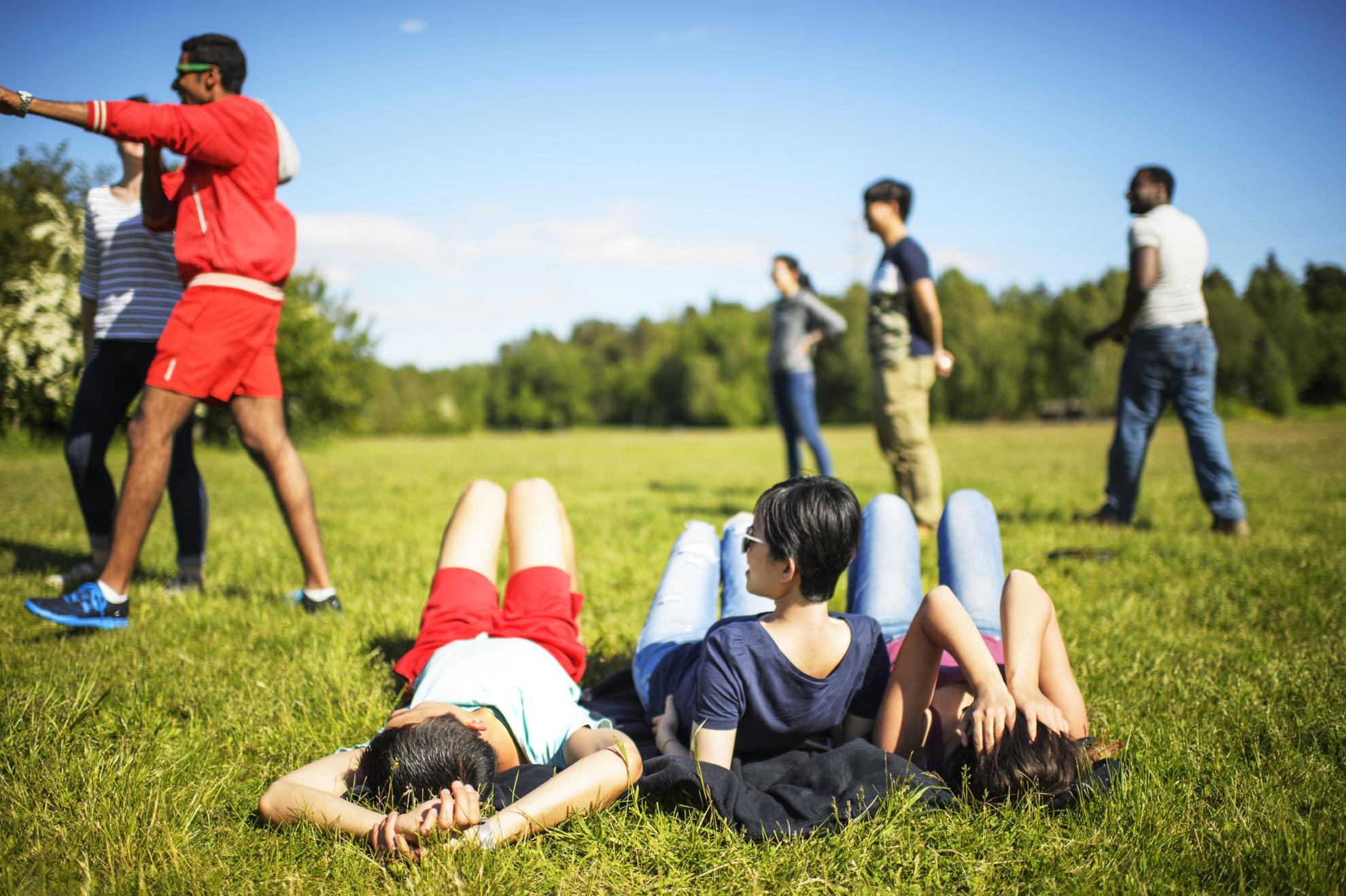 A group of young adults on the grass in a park, some lying down, others standing.