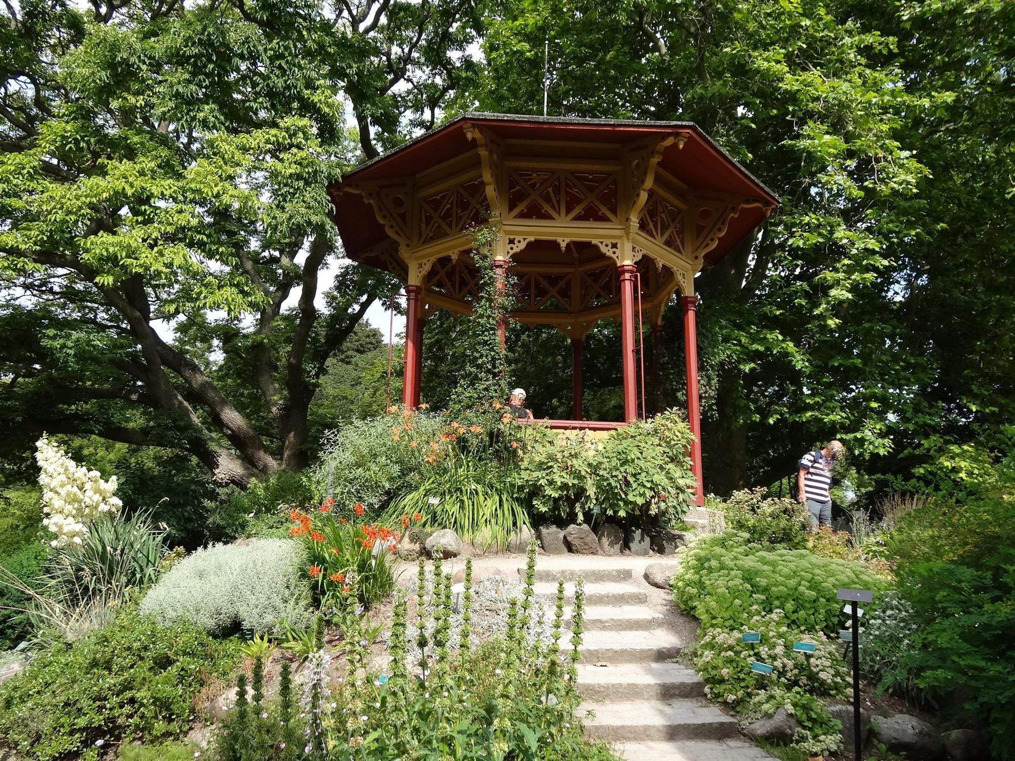 A red and yellow gazebo in a botanical garden during summer.