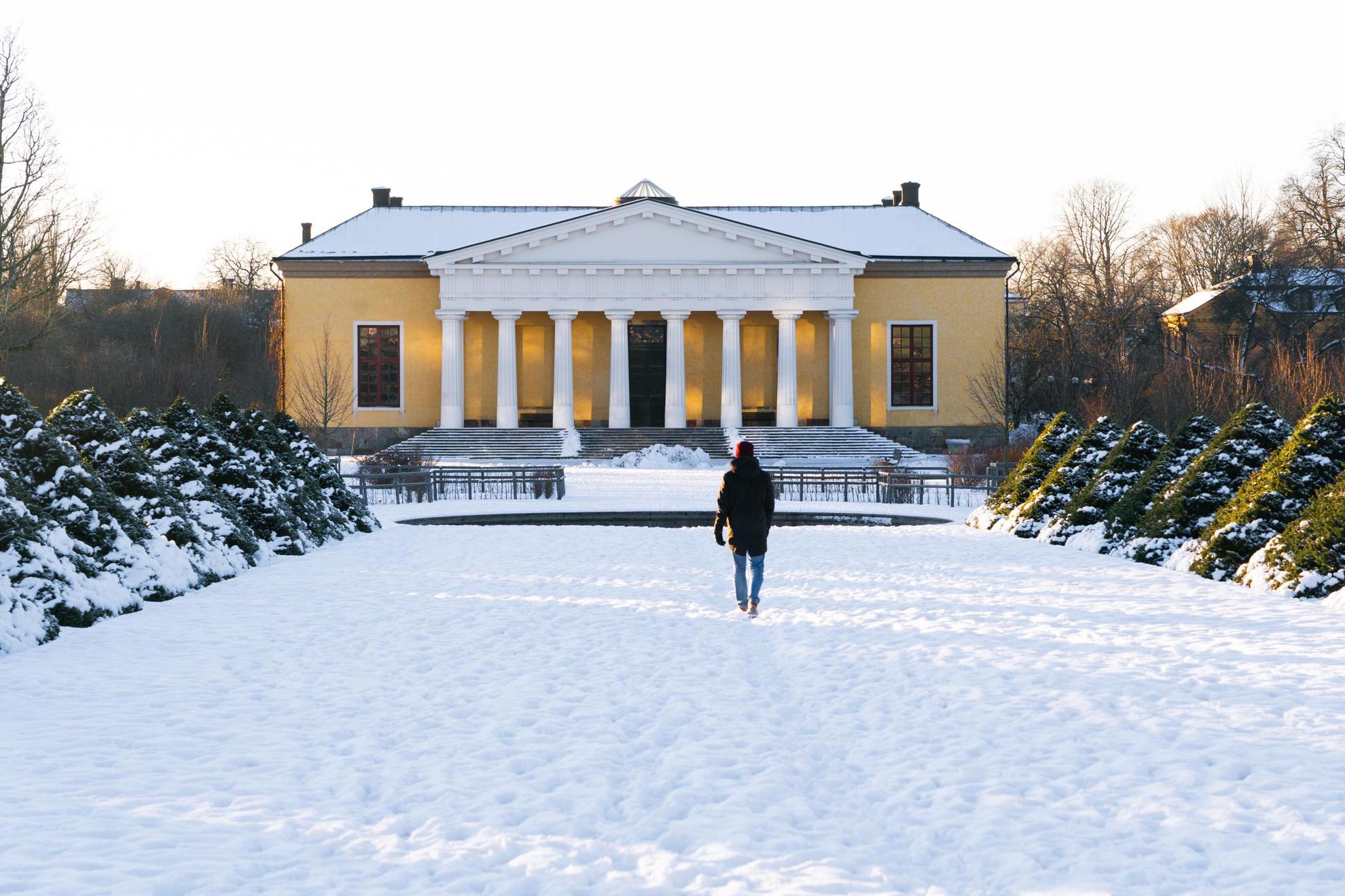 Une personne marchant vers une maison jaune au jardin botanique de l'Université d'Uppsala pendant l'hiver.