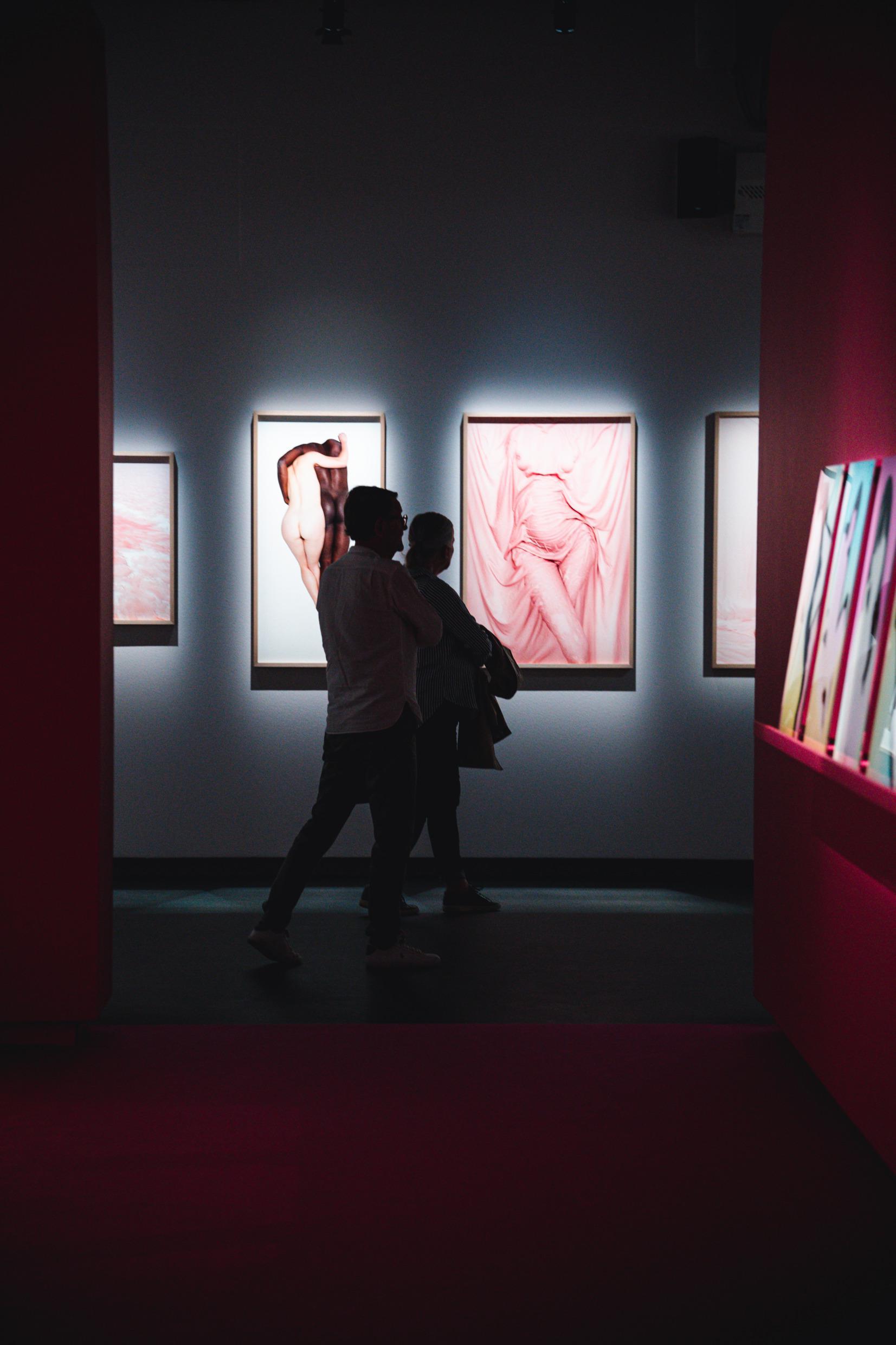 Deux personnes en train de marcher dans une salle d'expositions avec des photographies au mur.