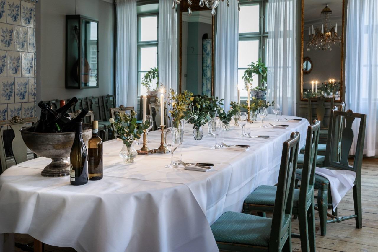 Une table dressée avec une nappe blanche, des couverts, des verres et des assiettes.